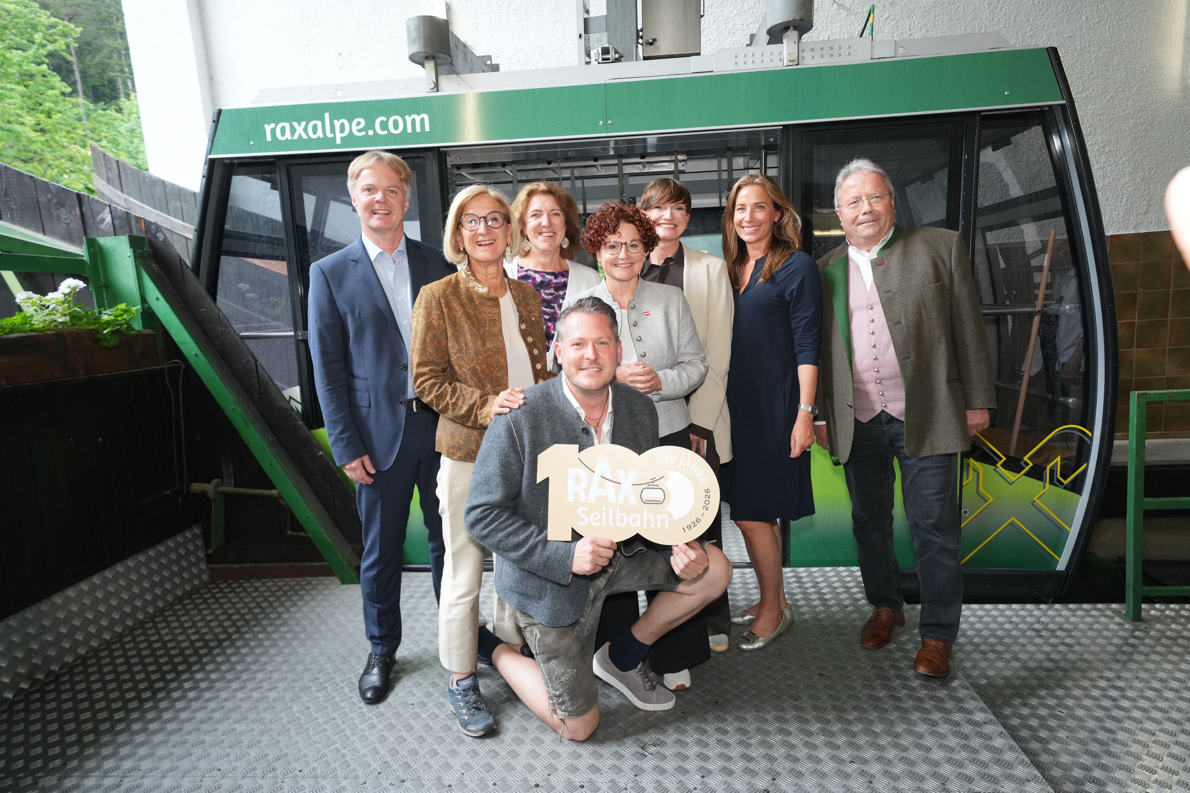 Acht Personen posieren vor einer Gondel der Rax-Seilbahn im Rahmen des Jubiläums 100 Jahre Rax-Seilbahn. 