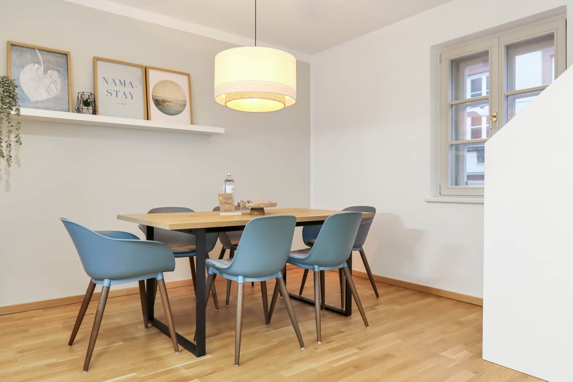 Large dining table with 6 chairs. There is a shelf with decorative elements and pictures on the wall.