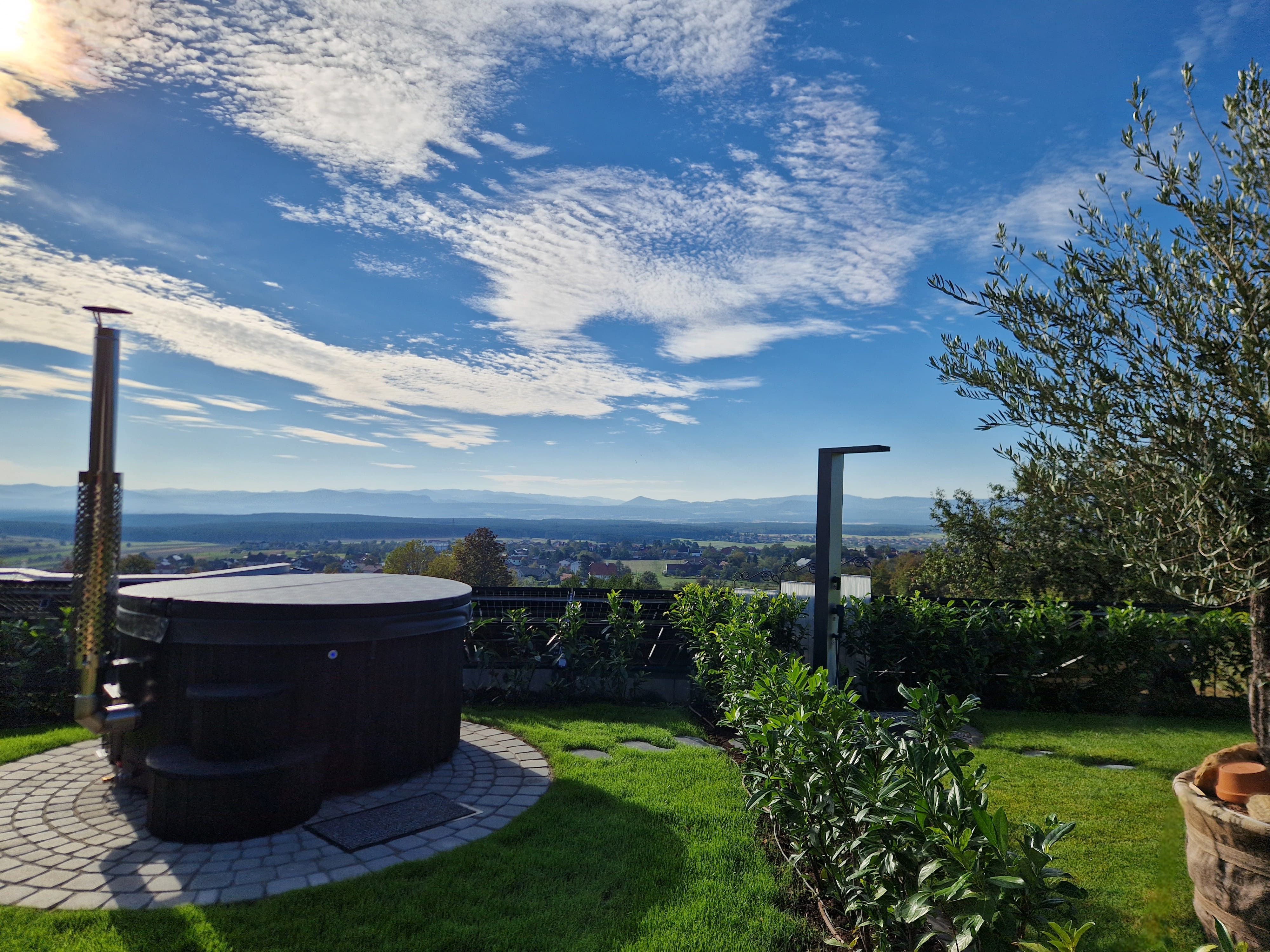 Ein runder Whirlpool im Garten mit Blick auf eine weite Landschaft und blauen Himmel.