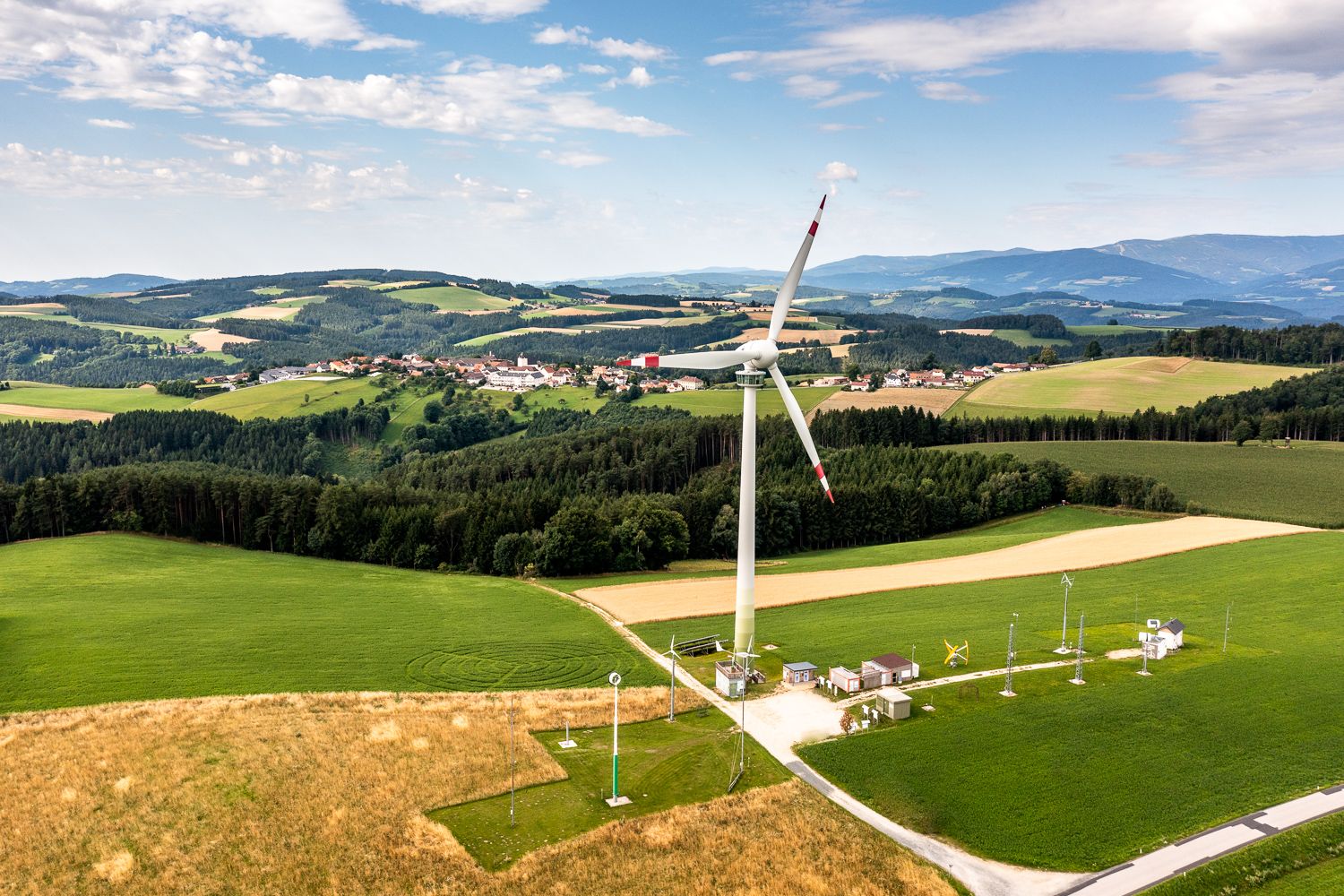Landschaft mit Windrad und Dorf im Hintergrund.