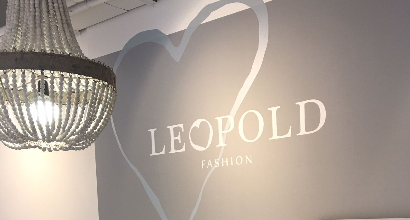 Ein Kronleuchter hängt vor einer grauen Wand mit der Aufschrift 'LEOPOLD FASHION' und einem Herzmotiv.