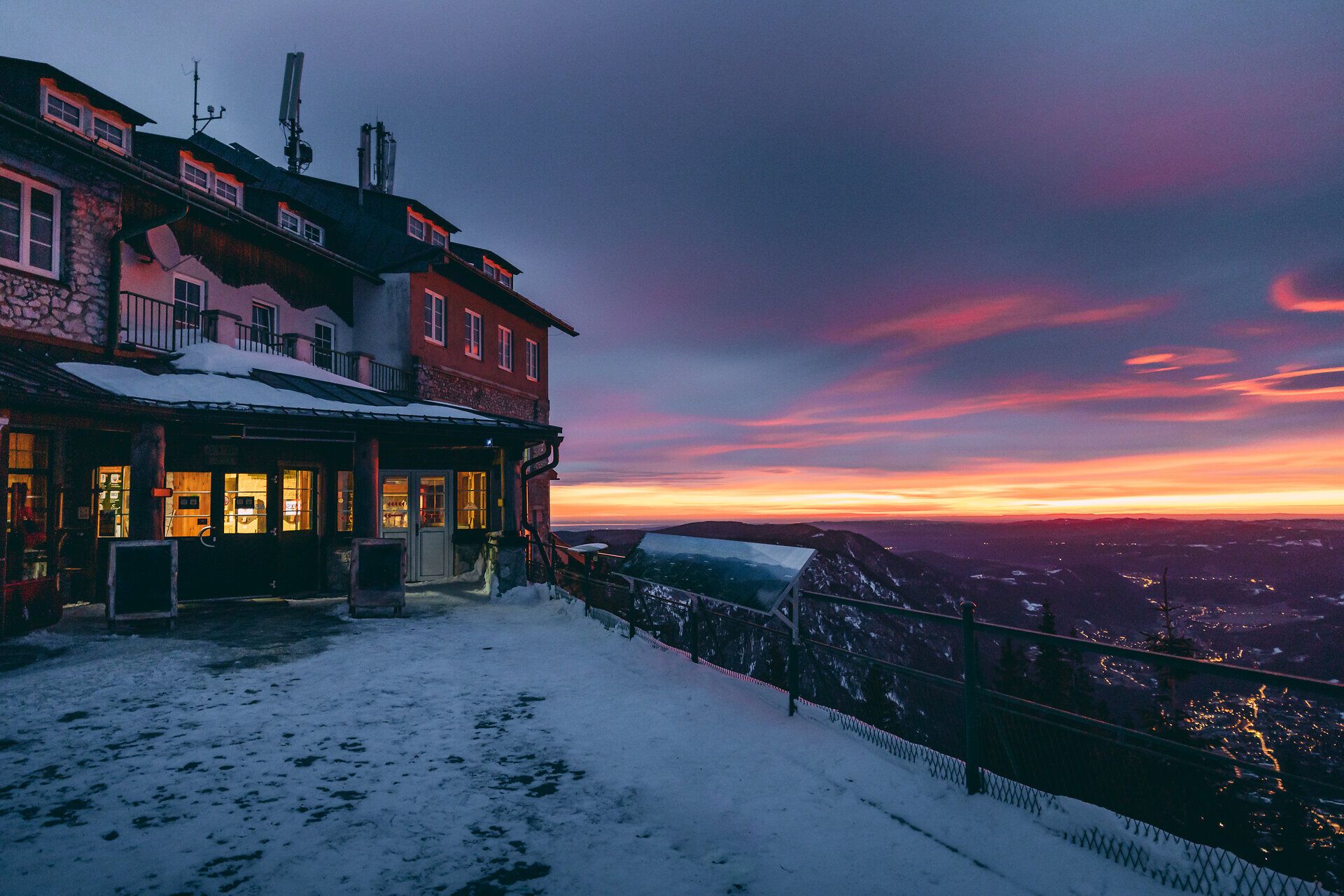 Die sanften Hügel der Wiener Alpen sind in eine traumhafte Schneedecke gehüllt, während die letzten Sonnenstrahlen den Himmel in ein spektakuläres Farbenspiel tauchen. Der Berggasthof Raxalpe lädt dazu ein, die winterliche Idylle zu genießen und die frische Bergluft zu atmen.