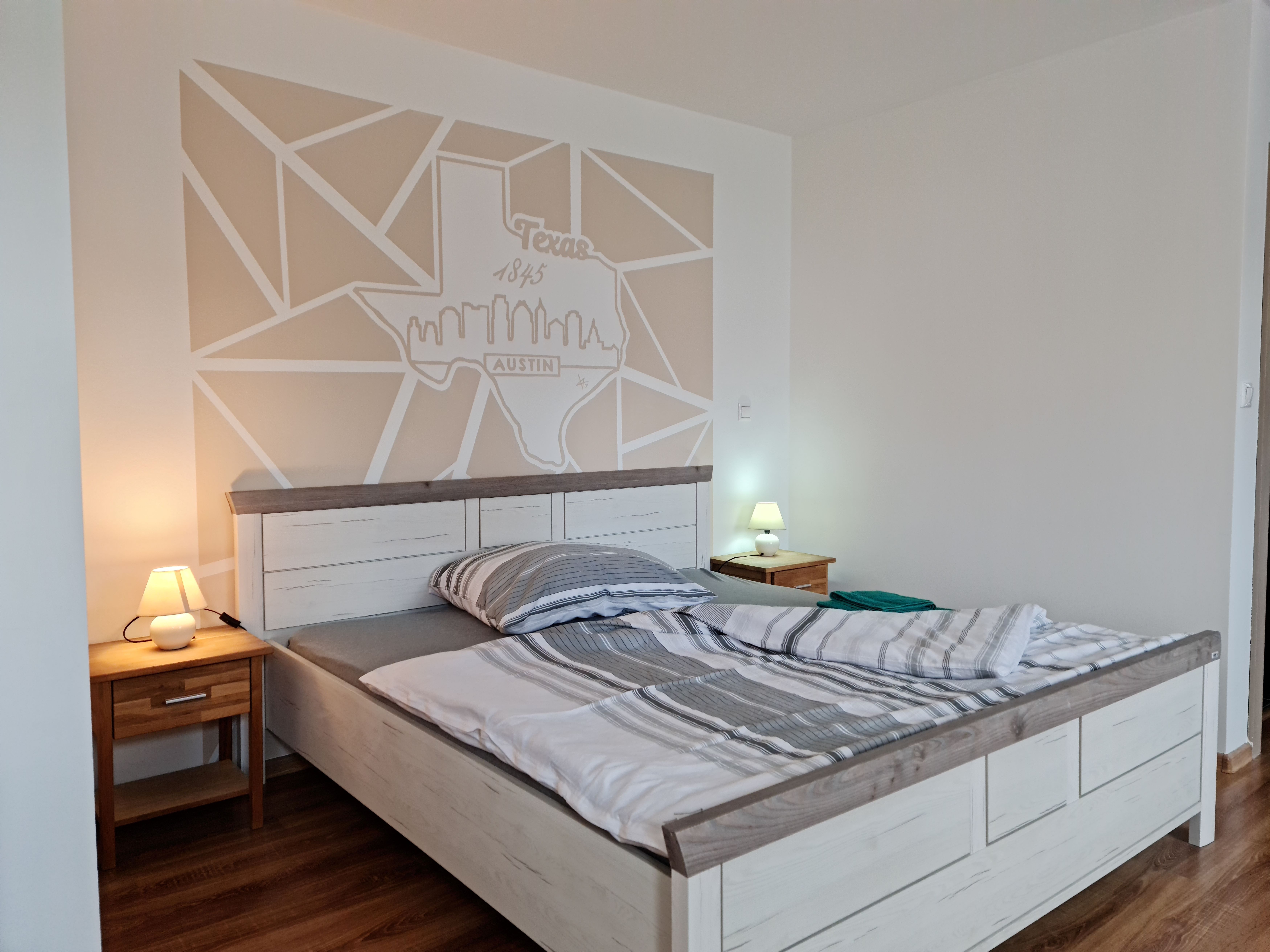 Ein gemütliches Schlafzimmer mit einem Doppelbett, zwei Nachttischen mit Lampen und einer Wanddekoration in Form der Texas-Karte mit Austin-Skyline.