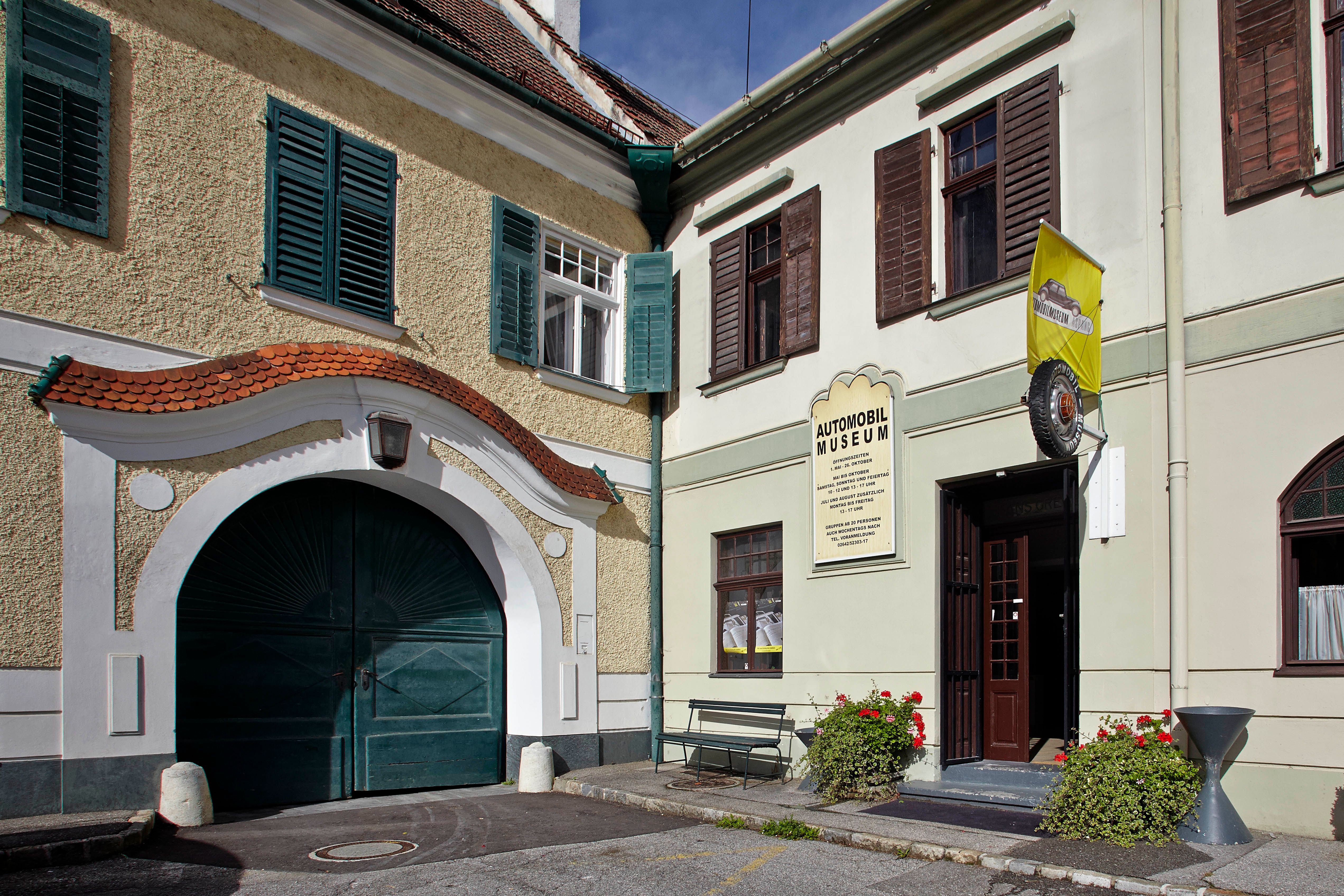 Eingang des Automobilmuseums Aspang Markt mit gelber Fahne und Blumen.
