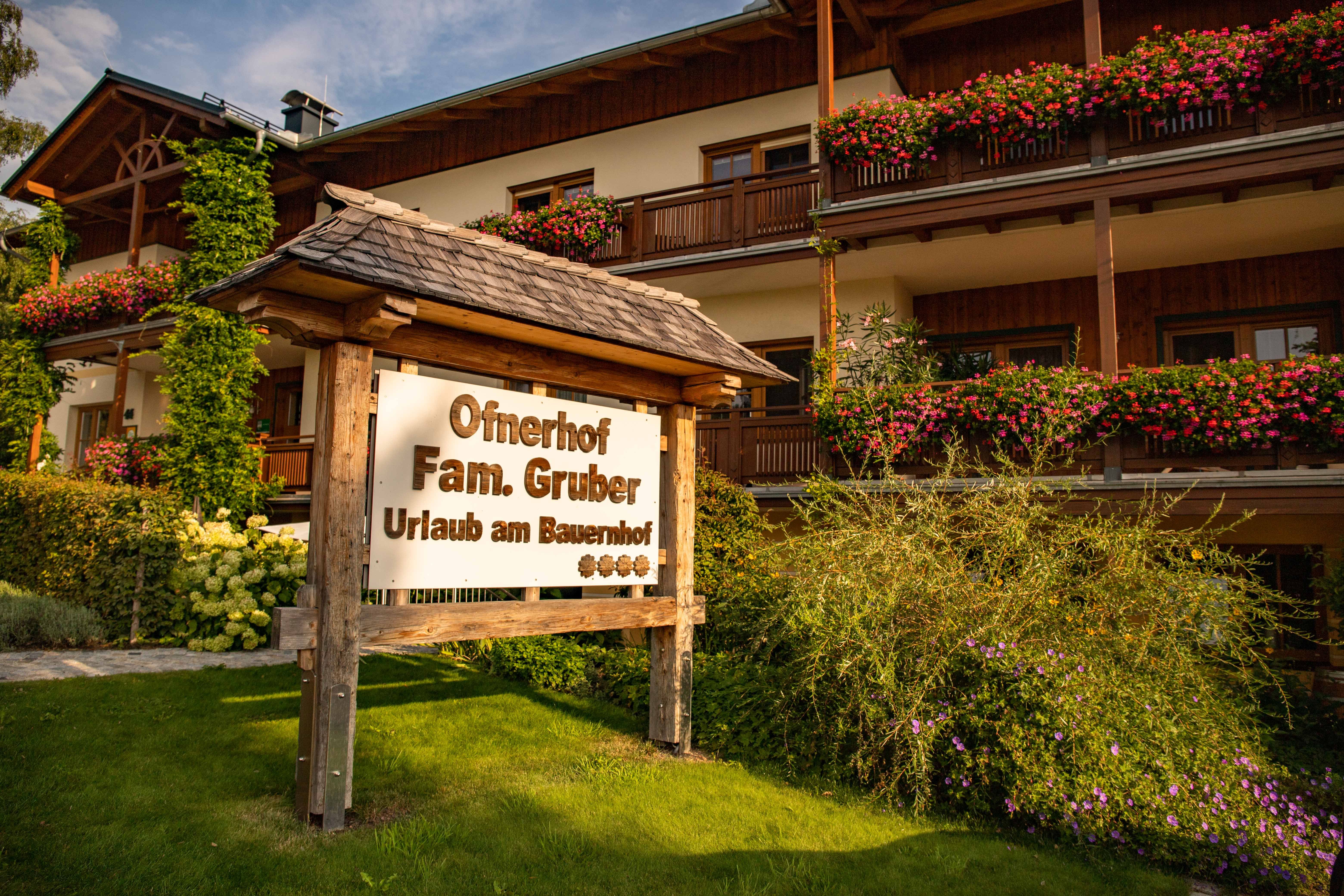 Schild vor einem Bauernhof mit Blumen und Holzveranda.