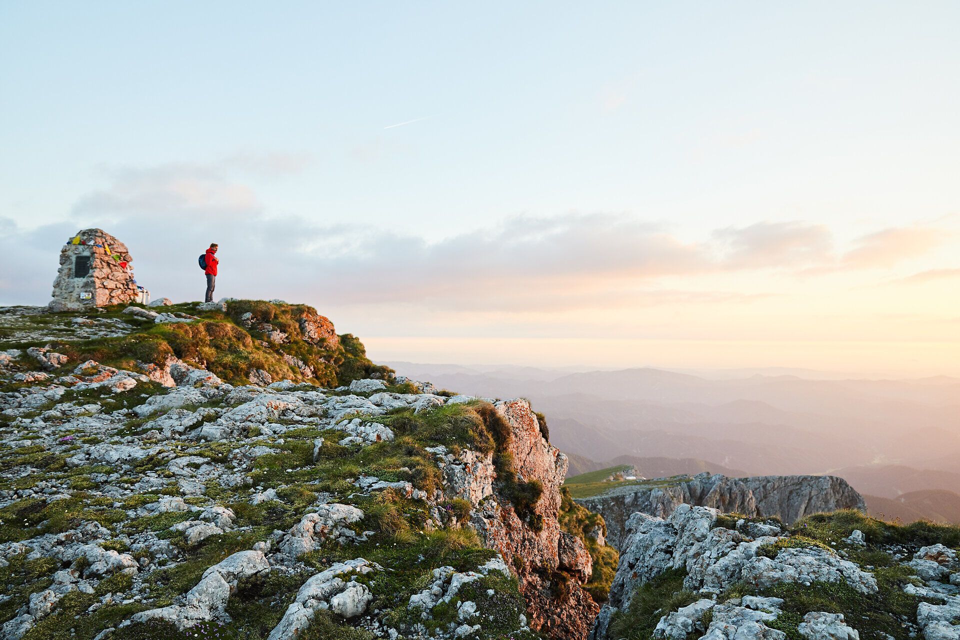 Die sanften Hügel des Schneebergs erstrahlen im warmen Licht der Abenddämmerung. Ein Wanderer genießt die atemberaubende Aussicht auf die umliegenden Berge und das weite Tal, während die Natur in voller Pracht erblüht.