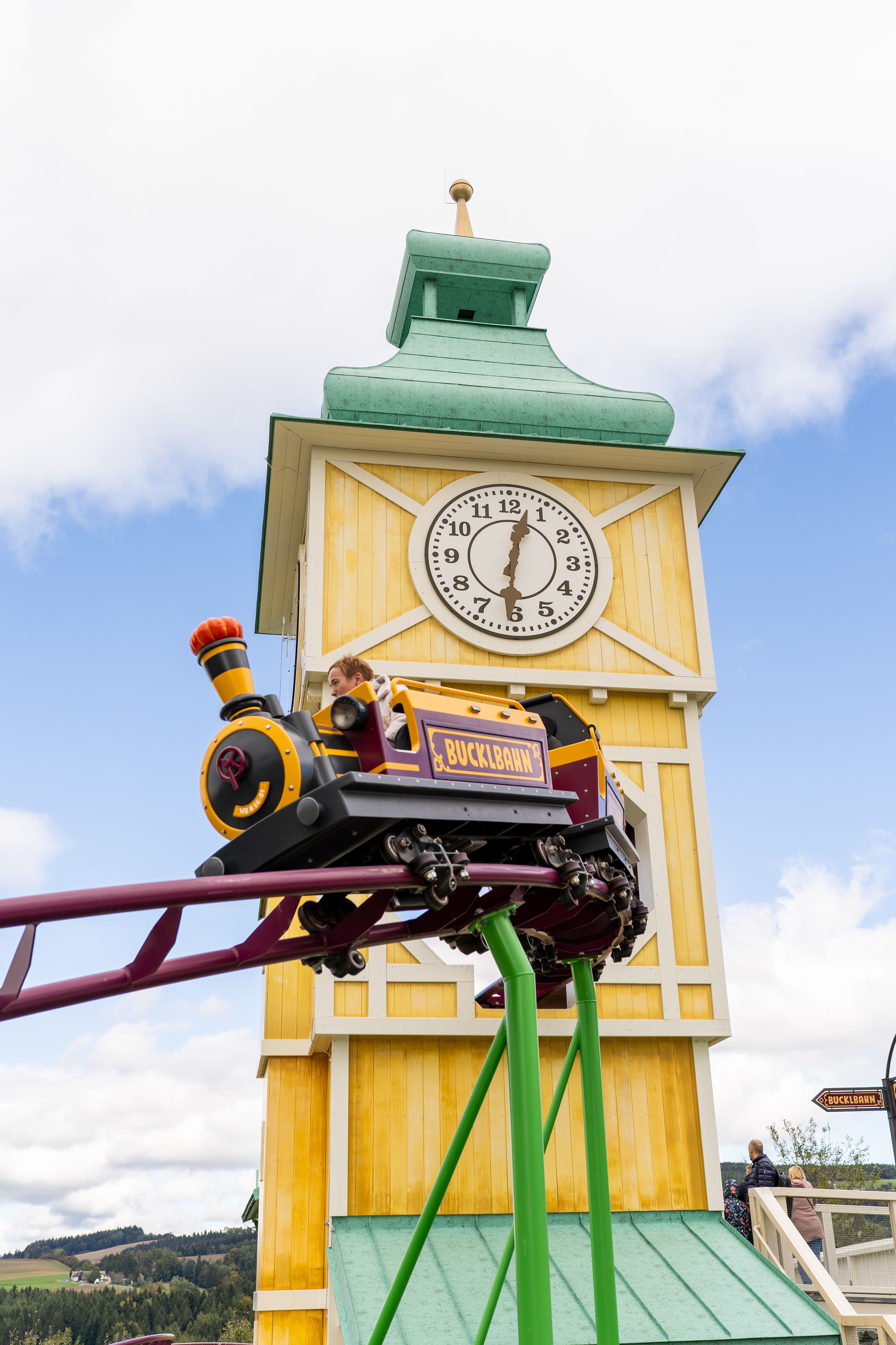 Eine Waggon der Achterbahn Bucklbahn im Eis-Greissler Erlebnispark, im Hintergrund gelber Turm mit Uhr.