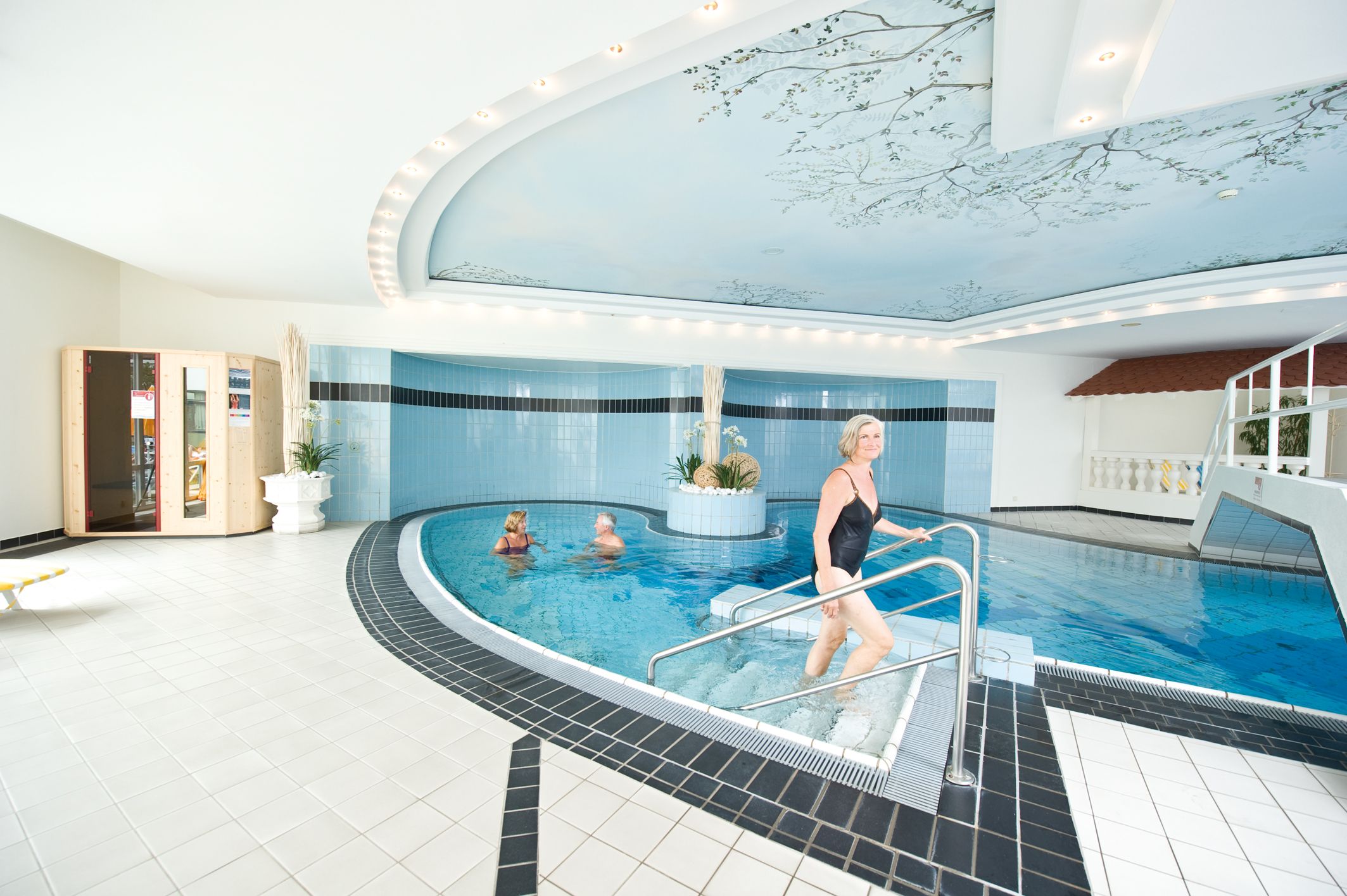 Innenpool mit Personen im Wasser und einer Frau, die die Treppe hinaufgeht.