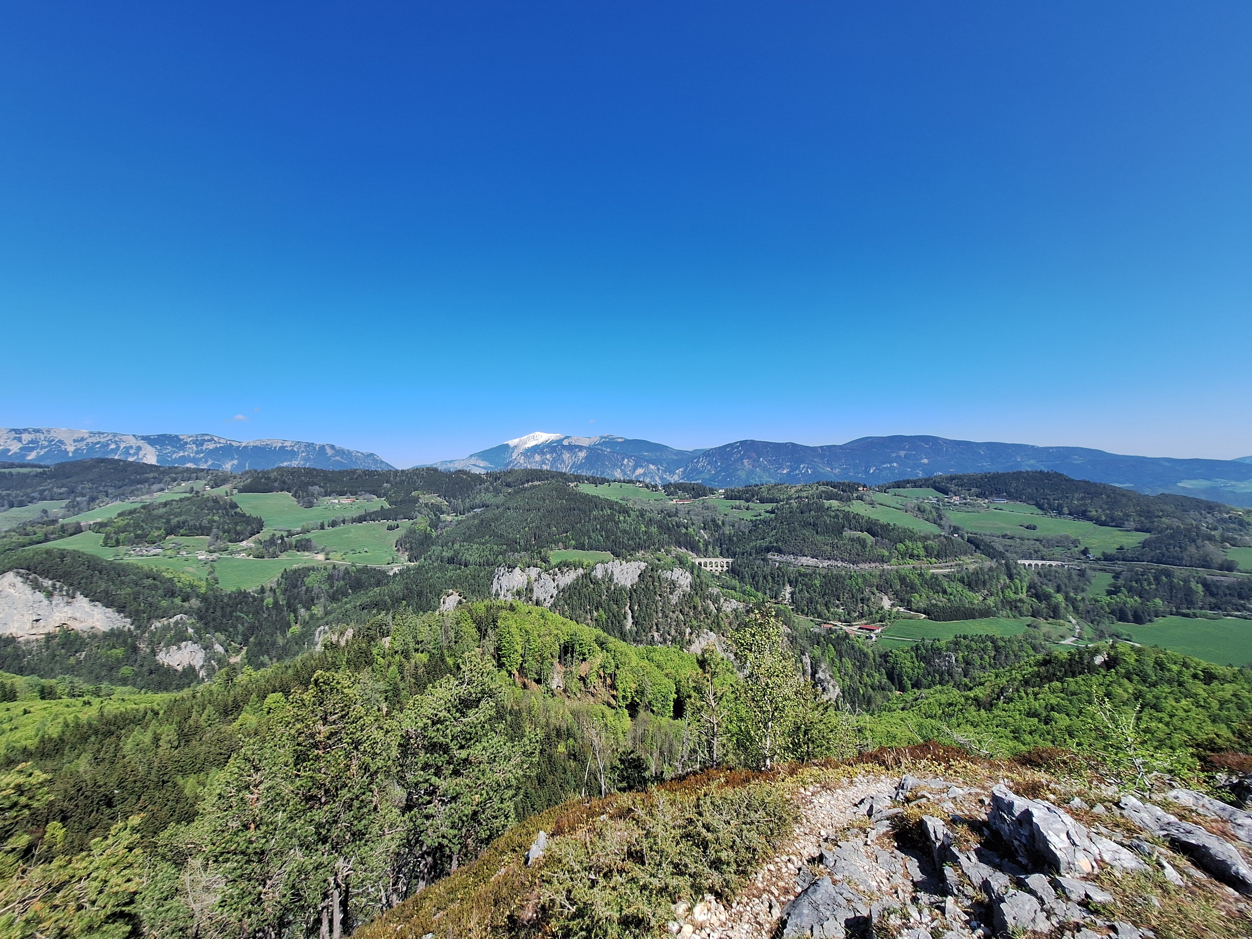 Ausblick vom Eselstein auf eine hügelige Berglandschaft mit Blick auf die Rax und den Schneeberg