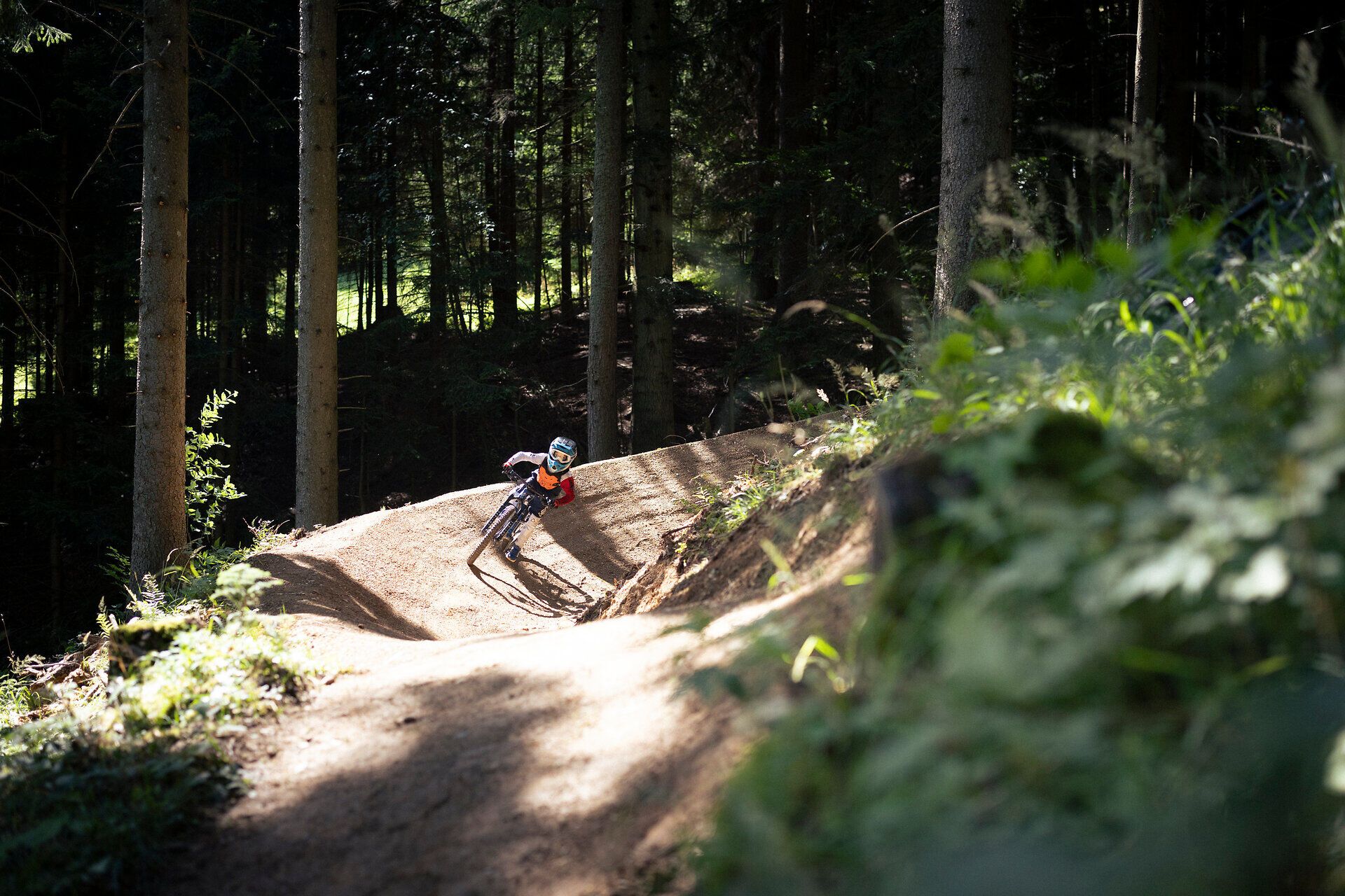 Mountainbiken im Alpenbikepark Puchberg am Schneeberg in Niederösterreich: Kind fährt mit dem Mountainbike durch eine steile Anliegerkurve auf einem Waldtrail in den Wiener Alpen.
