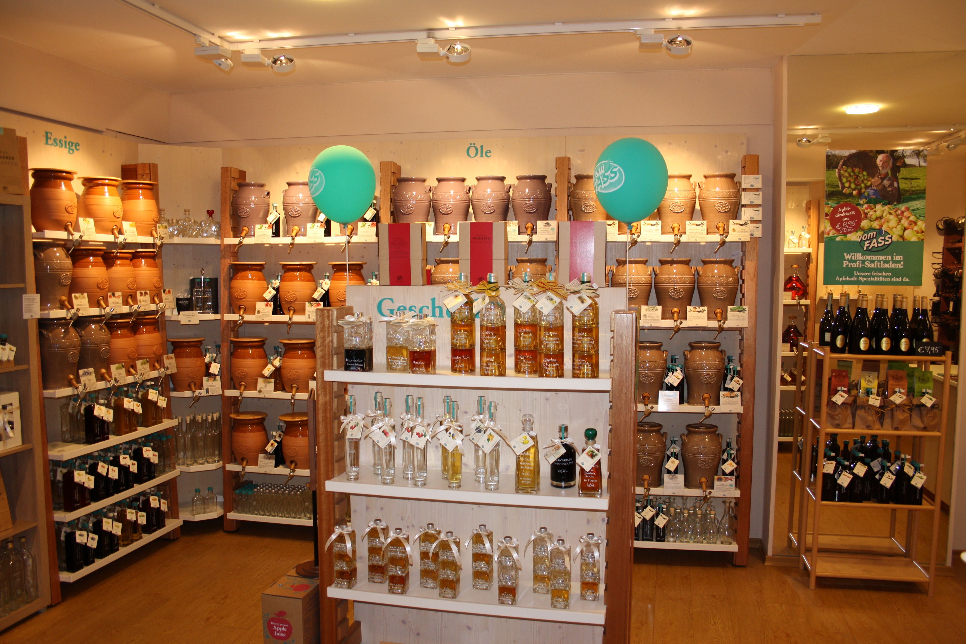 Ein Laden mit Regalen voller Essig- und Ölkrüge sowie Flaschen, dekoriert mit grünen Luftballons.