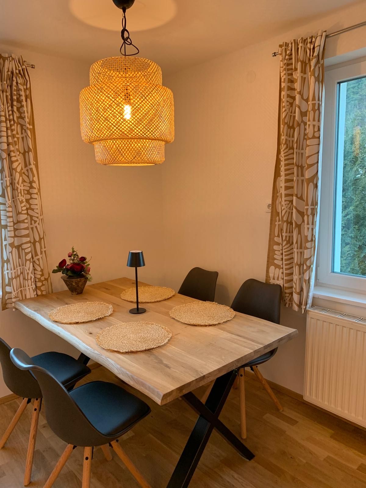 Essbereich mit Holztisch, vier schwarzen Stühlen, runder Lampe und Fenster mit Vorhängen.