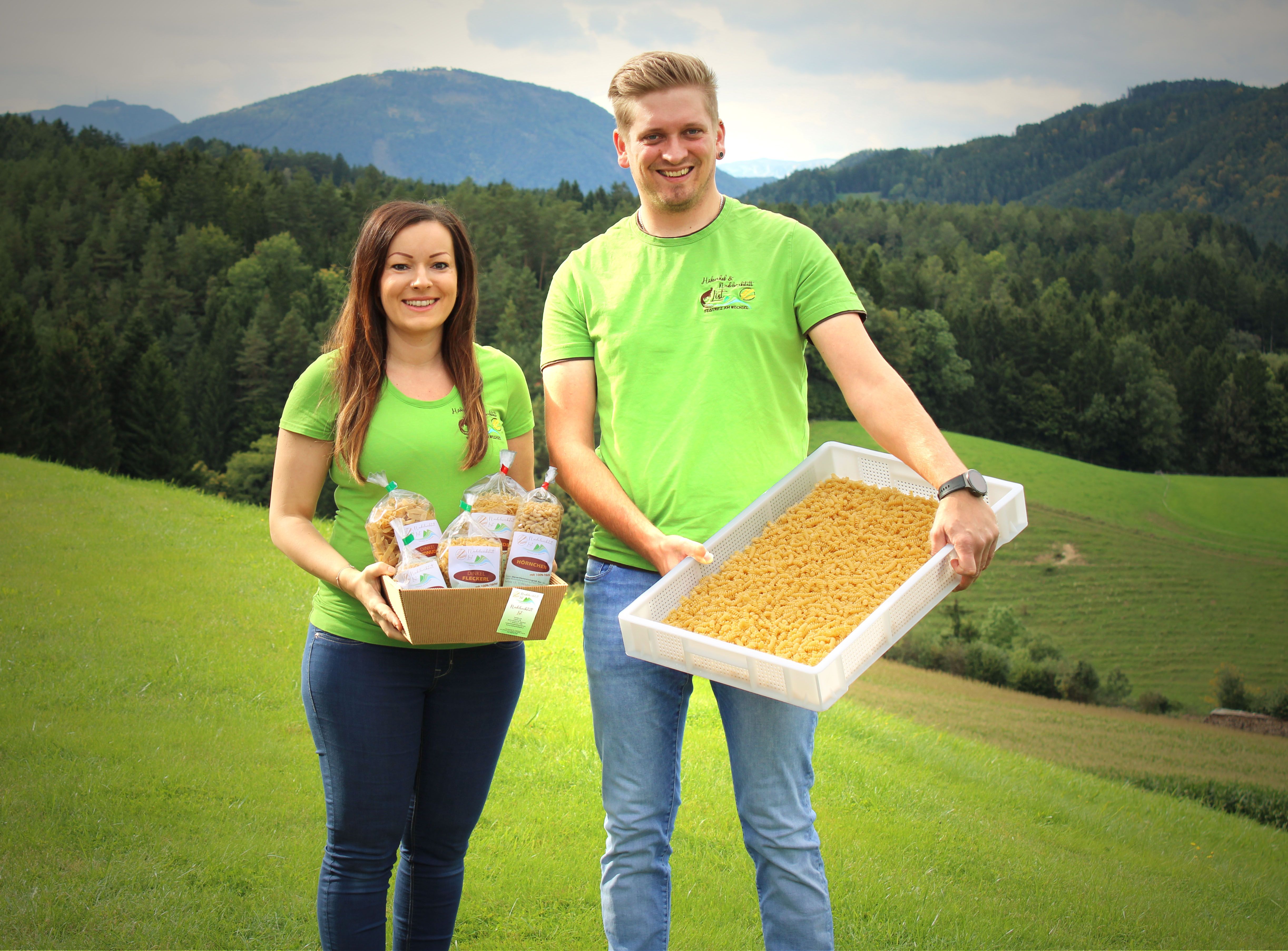 Ein Mann und eine Frau mit grünen T-Shirts stehen auf einer grünen Wiese und halten Nudelprodukte.