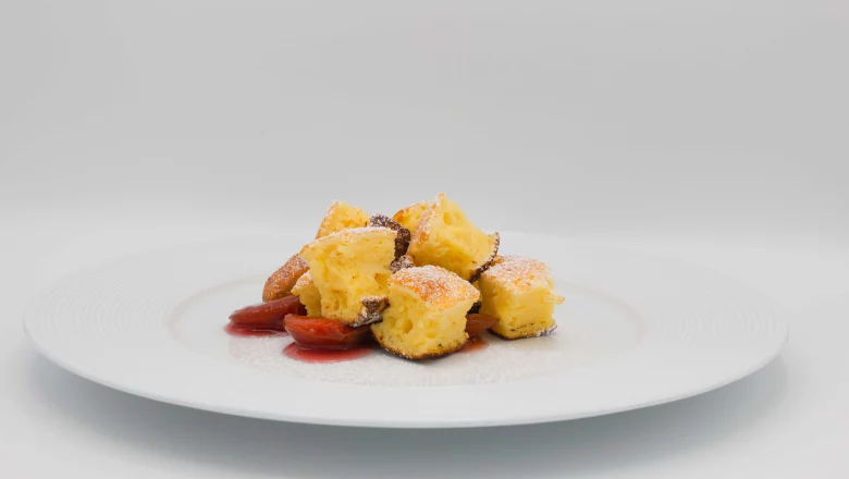 Ein Teller mit Sauerrahmschmarrn und Zwetschkenröster vor weißem Hintergrund. 