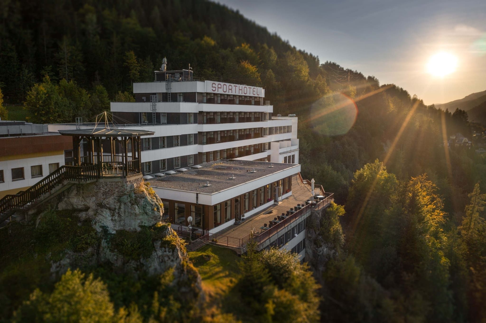 Außenansicht des Sporthotels Semmering bei Sonnenuntergang, umgeben von Wald.