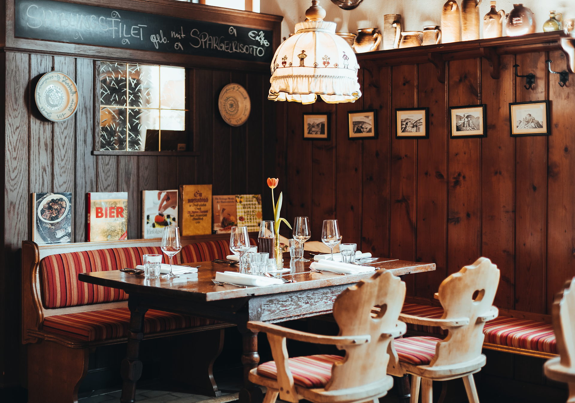 In einem einladenden Wirtshaus mit rustikalem Charme erwartet die Gäste eine gemütliche Atmosphäre. Der Tisch ist liebevoll gedeckt, während sanftes Licht von der Deckenlampe auf die Holzvertäfelung fällt. Hier lässt sich der Tag bei regionalen Köstlichkeiten und einem Glas Cider wunderbar ausklingen.