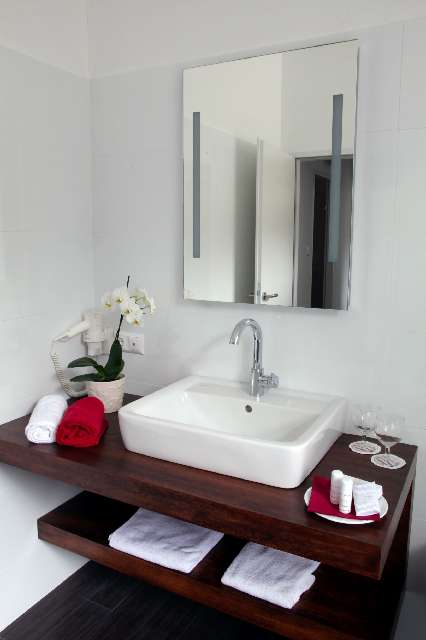 Modernes Badezimmer mit Waschbecken, Spiegel, Handtüchern und Orchidee.