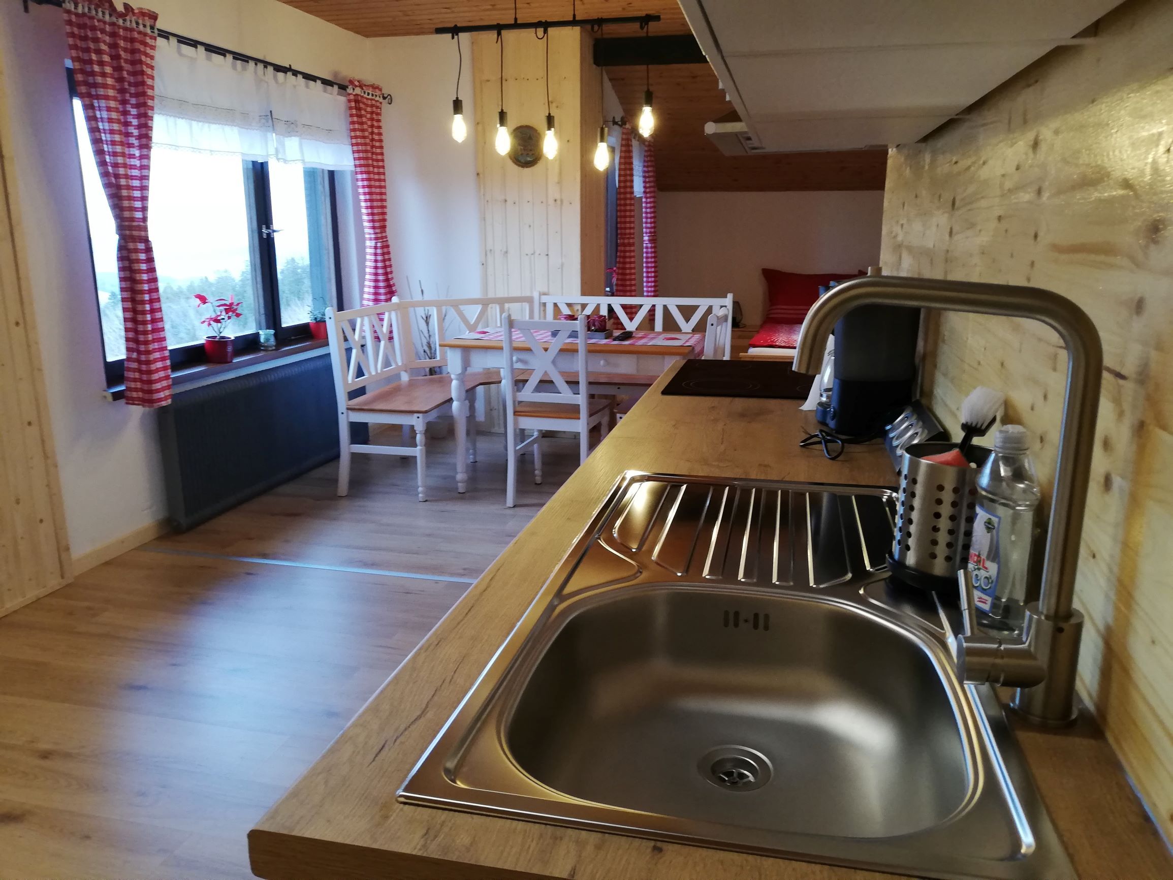 Küche in einem Dachgeschoss-Apartment mit Holzverkleidung, Spüle, Esstisch und roten Vorhängen.