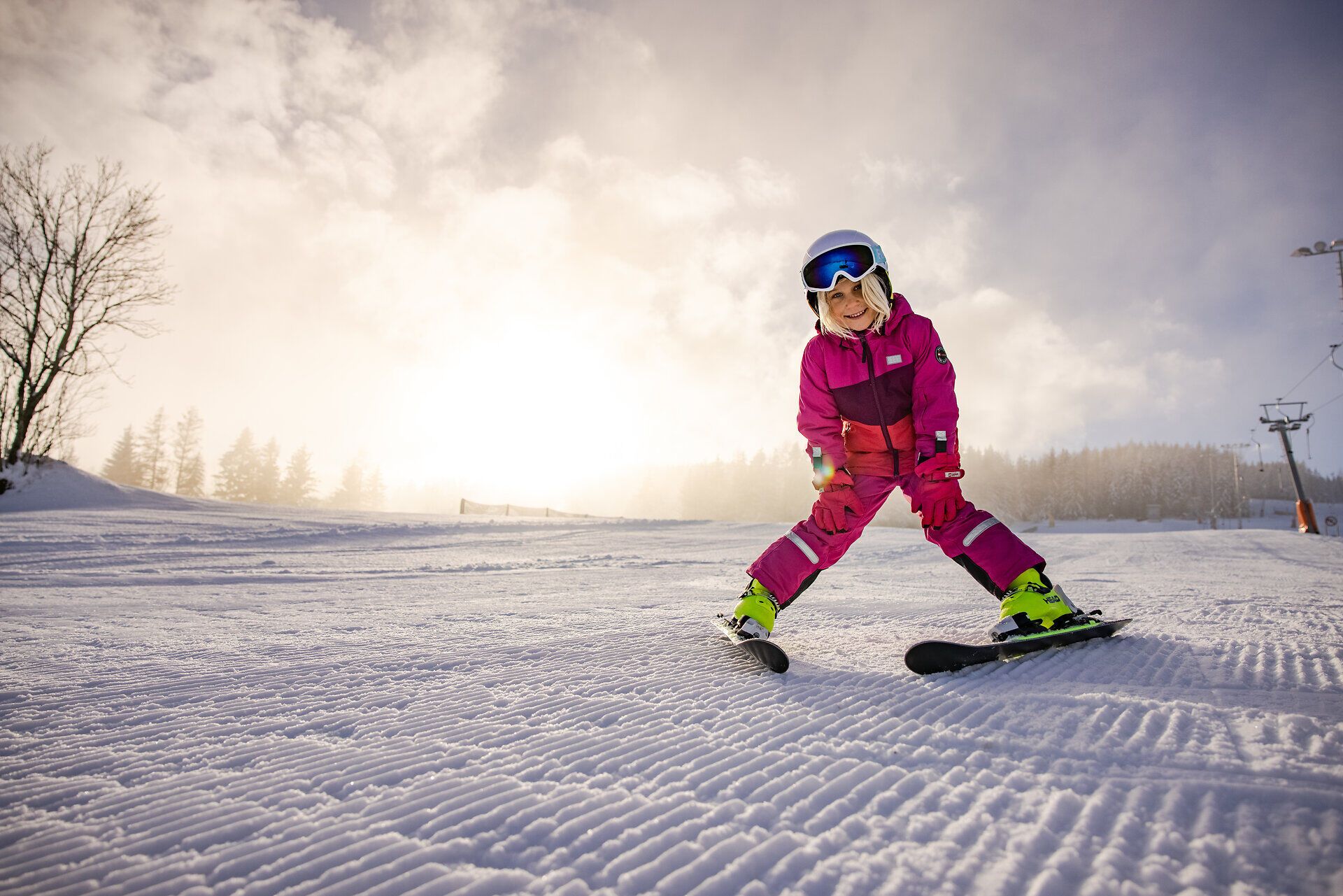 Kind in pinkem Skianzug fährt auf einer frisch präparierten Skipiste