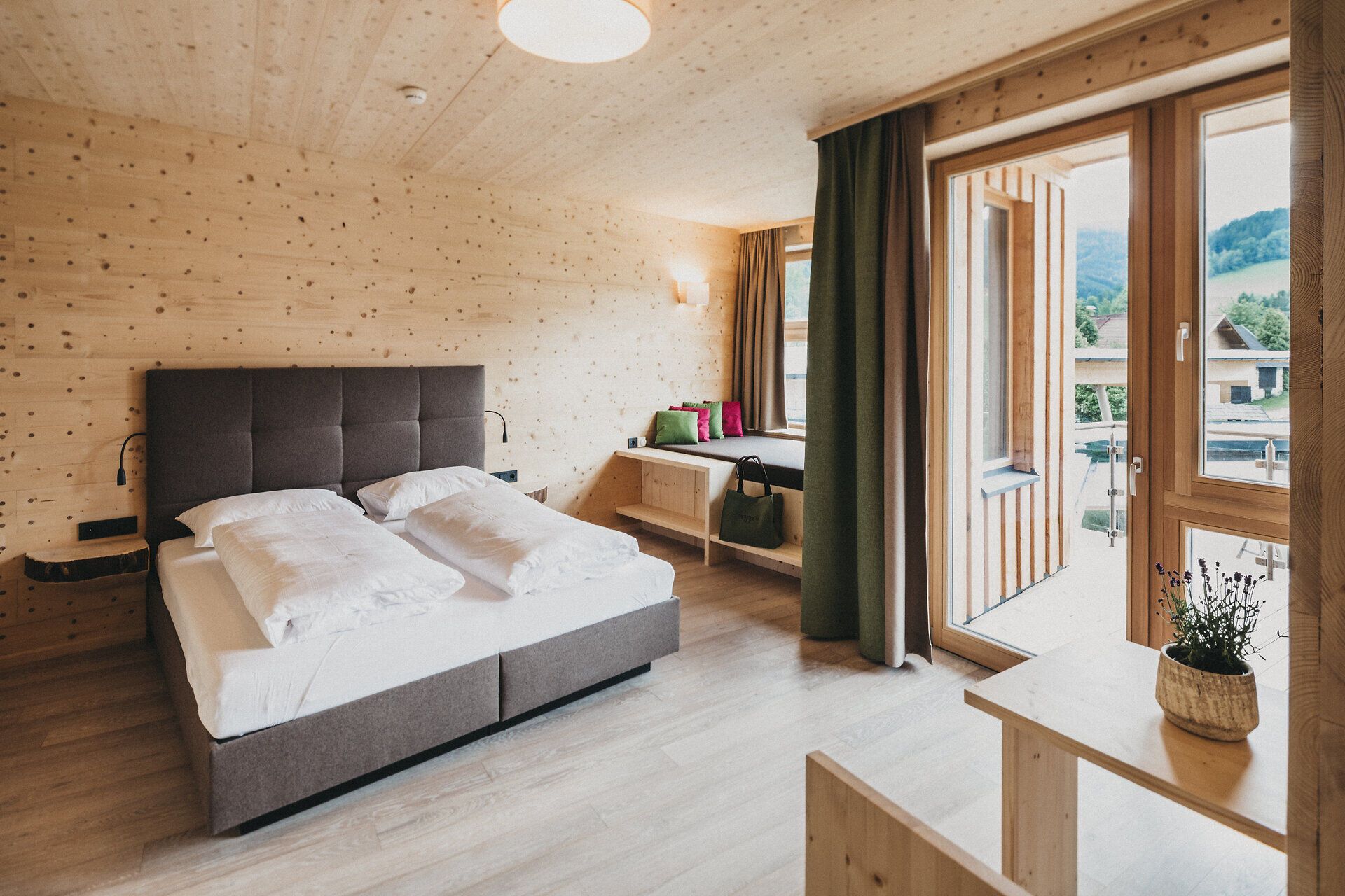 In einem stilvollen Zimmer mit warmen Holzwänden und einem gemütlichen Doppelbett lädt die ruhige Atmosphäre zum Entspannen ein. Große Fenster bieten einen herrlichen Blick auf die umliegende Natur und lassen viel Tageslicht herein, während die geschmackvolle Einrichtung ein Gefühl von Heimatlichkeit vermittelt.