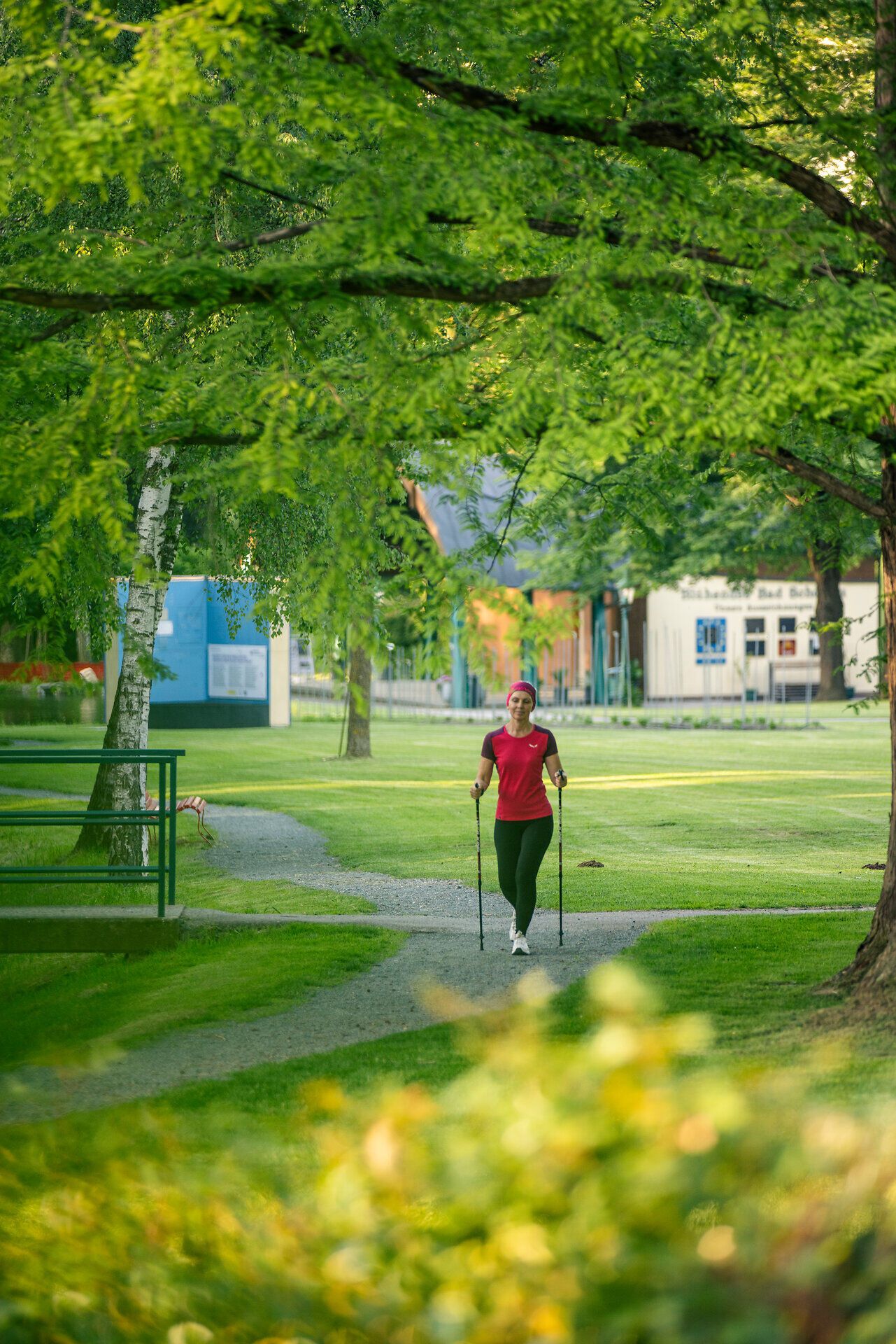 Eine sportlich gekleidete Frau geht mit Walkingstöcken durch den Kurpark Bad Schönau.