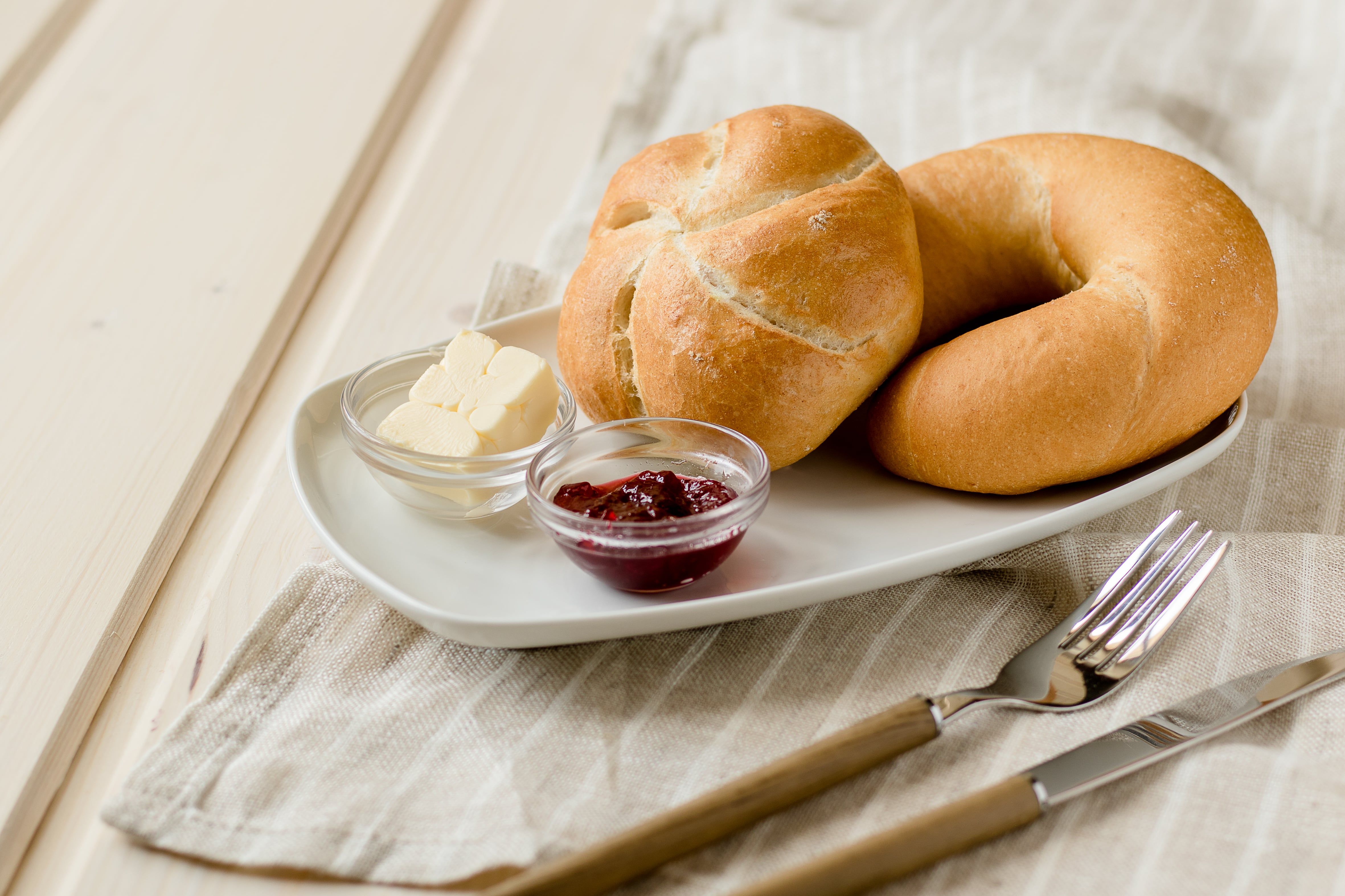 Frühstücksteller mit Brötchen, Butter und Marmelade auf einem Tisch.