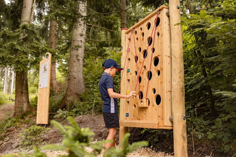 Ein Junge spielt an einer hölzernen Kugelbahn im Wald.
