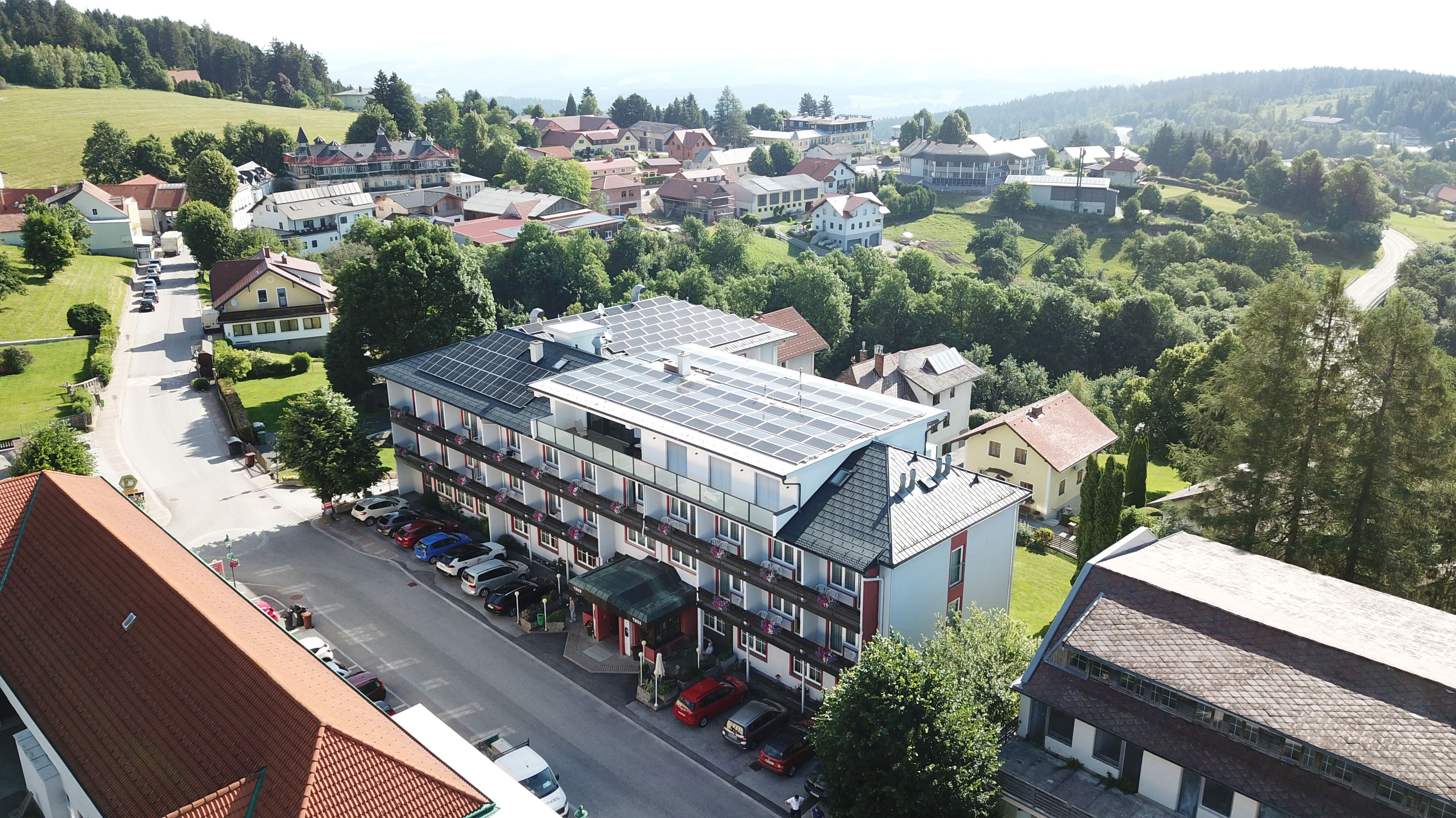 Luftaufnahme eines Hotels mit Solarpanelen auf dem Dach, umgeben von Bäumen und weiteren Gebäuden in einer ländlichen Gegend.