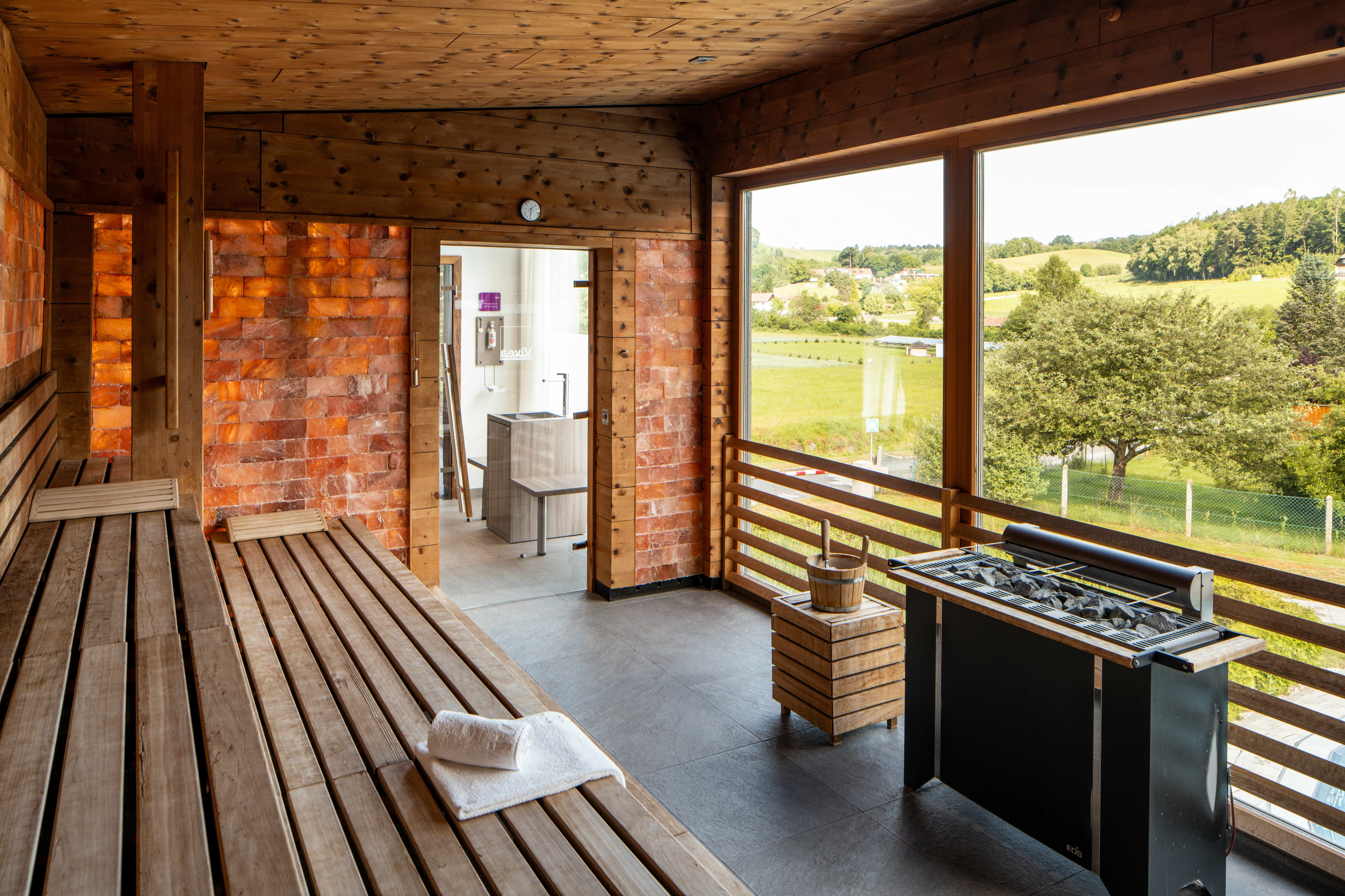 Innenansicht einer Sauna mit Holzbänken und einem großen Fenster mit Blick auf eine grüne Landschaft.