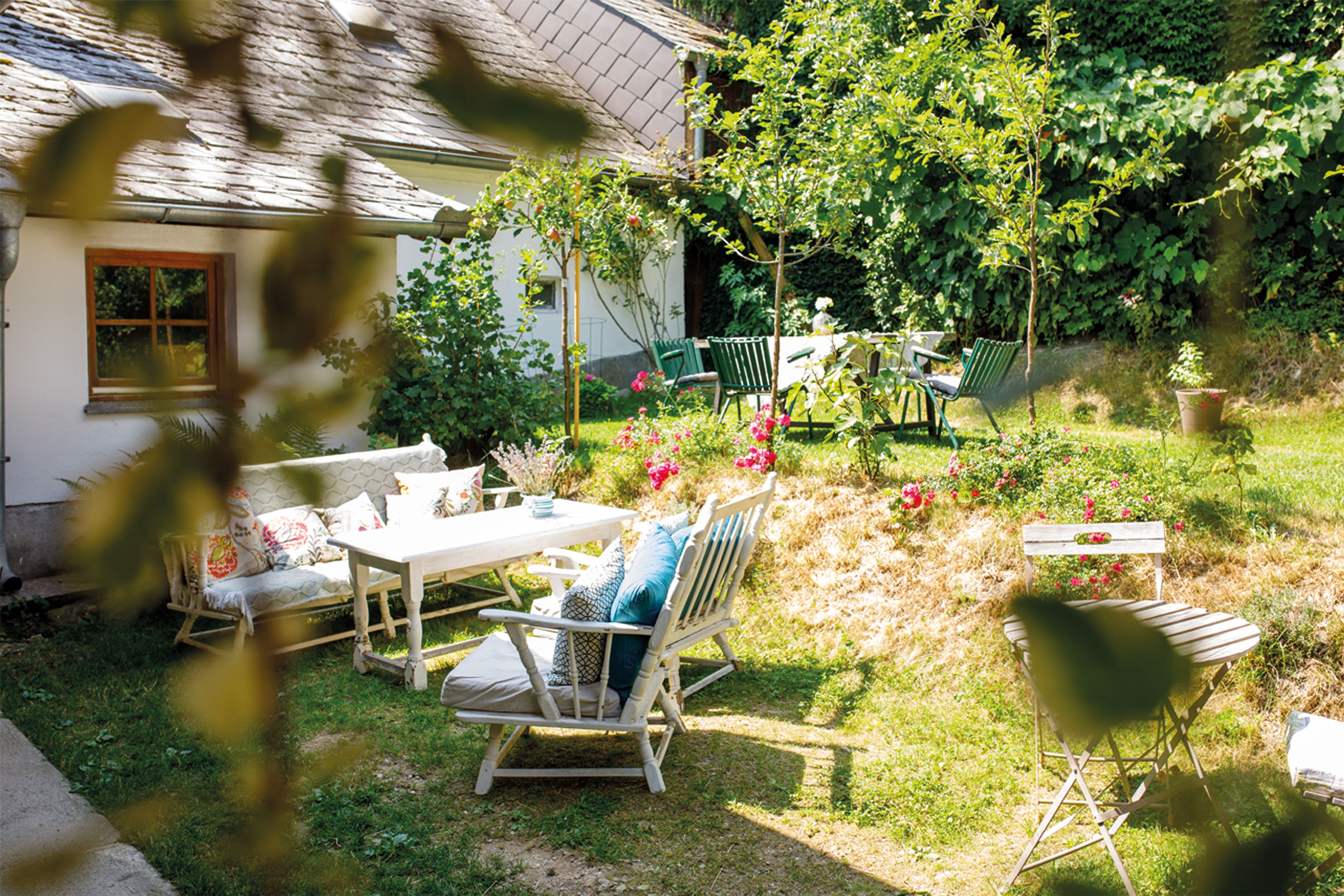 Ein gemütlicher Garten mit Sitzmöbeln, Blumen und Bäumen vor einem Haus.