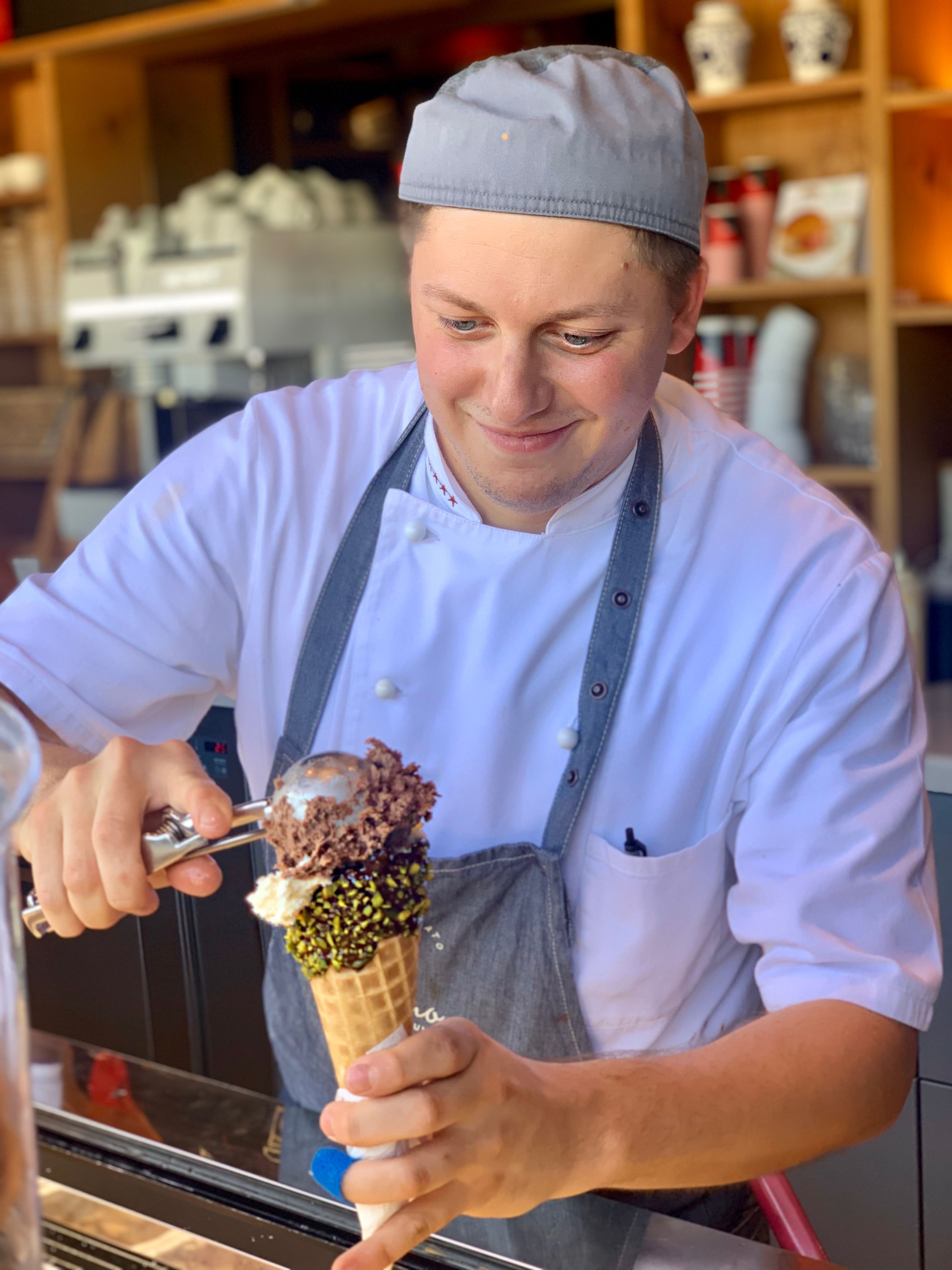 Eine Eisverkäuferin serviert eine Pistazientüte mit Schokoladeneis.