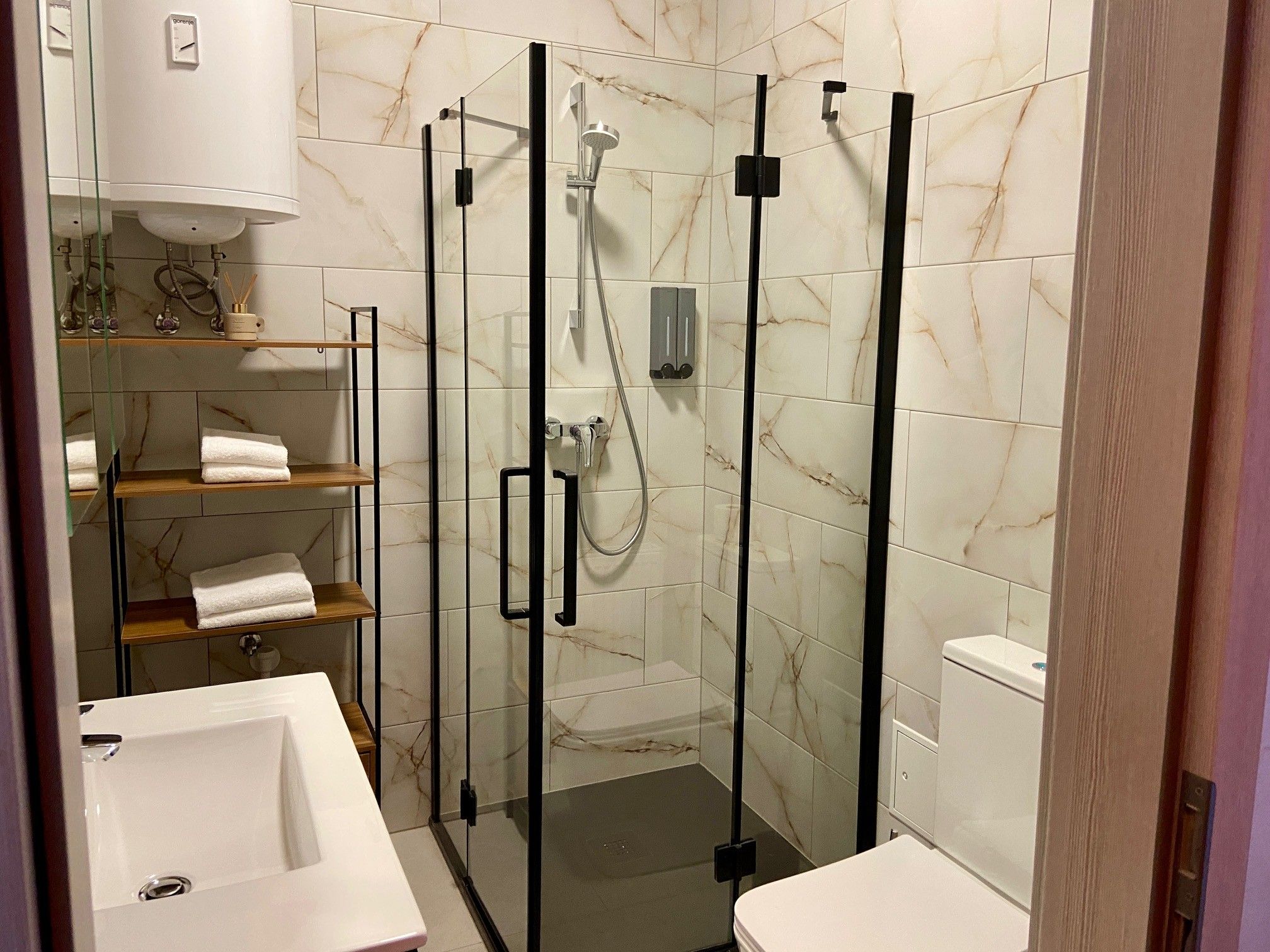 Modernes Badezimmer mit Glasdusche, Waschbecken, WC und Regal mit Handtüchern.