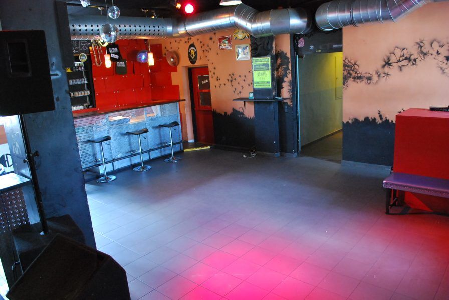 Innenansicht eines leeren Nachtclubs mit Bar, Hockern und Lüftungsrohren.