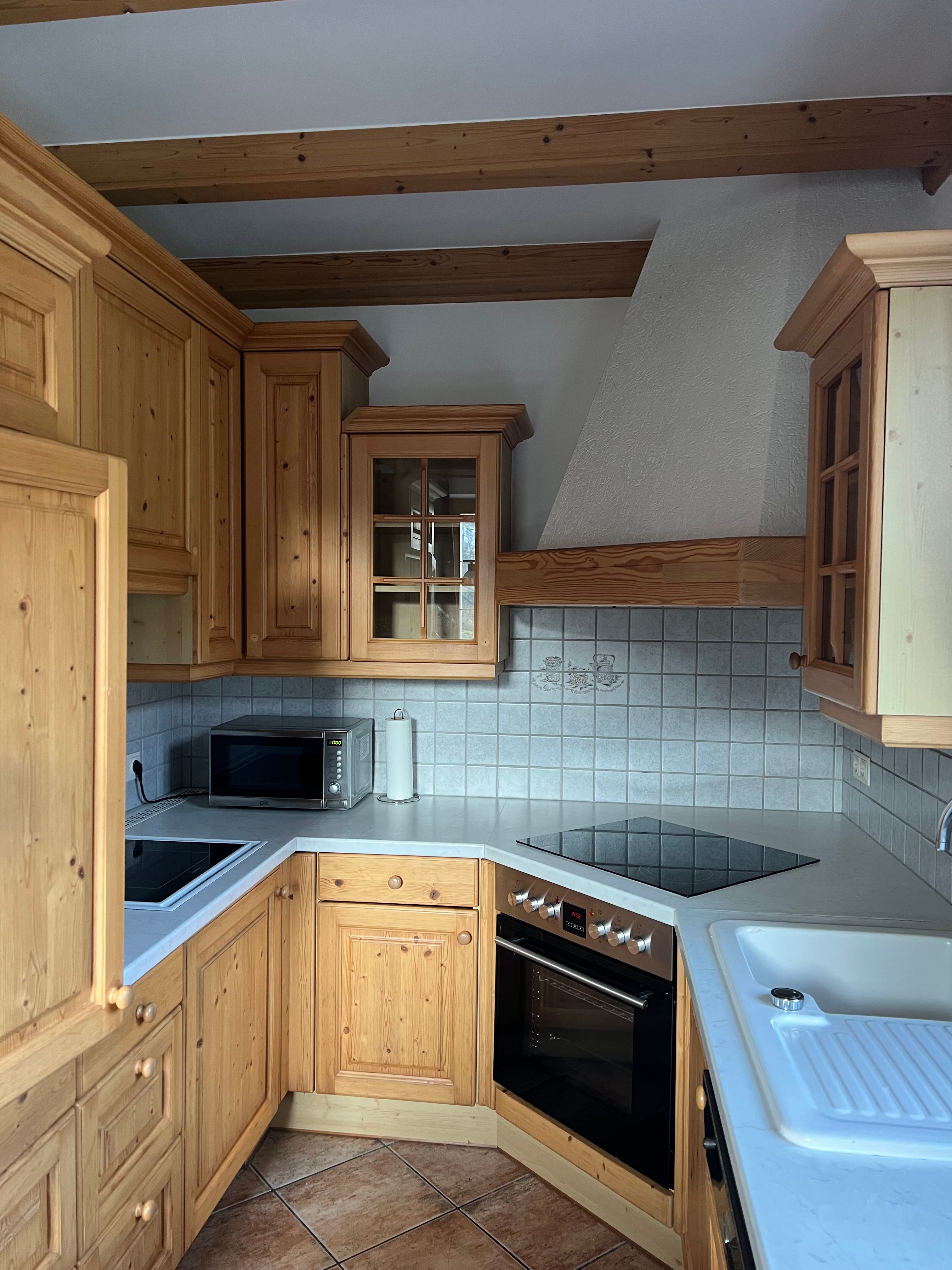 Eine rustikale Küche mit Holzschränken, einem Elektroherd, einer Mikrowelle und einem Waschbecken. Die Wände sind mit Fliesen verkleidet.