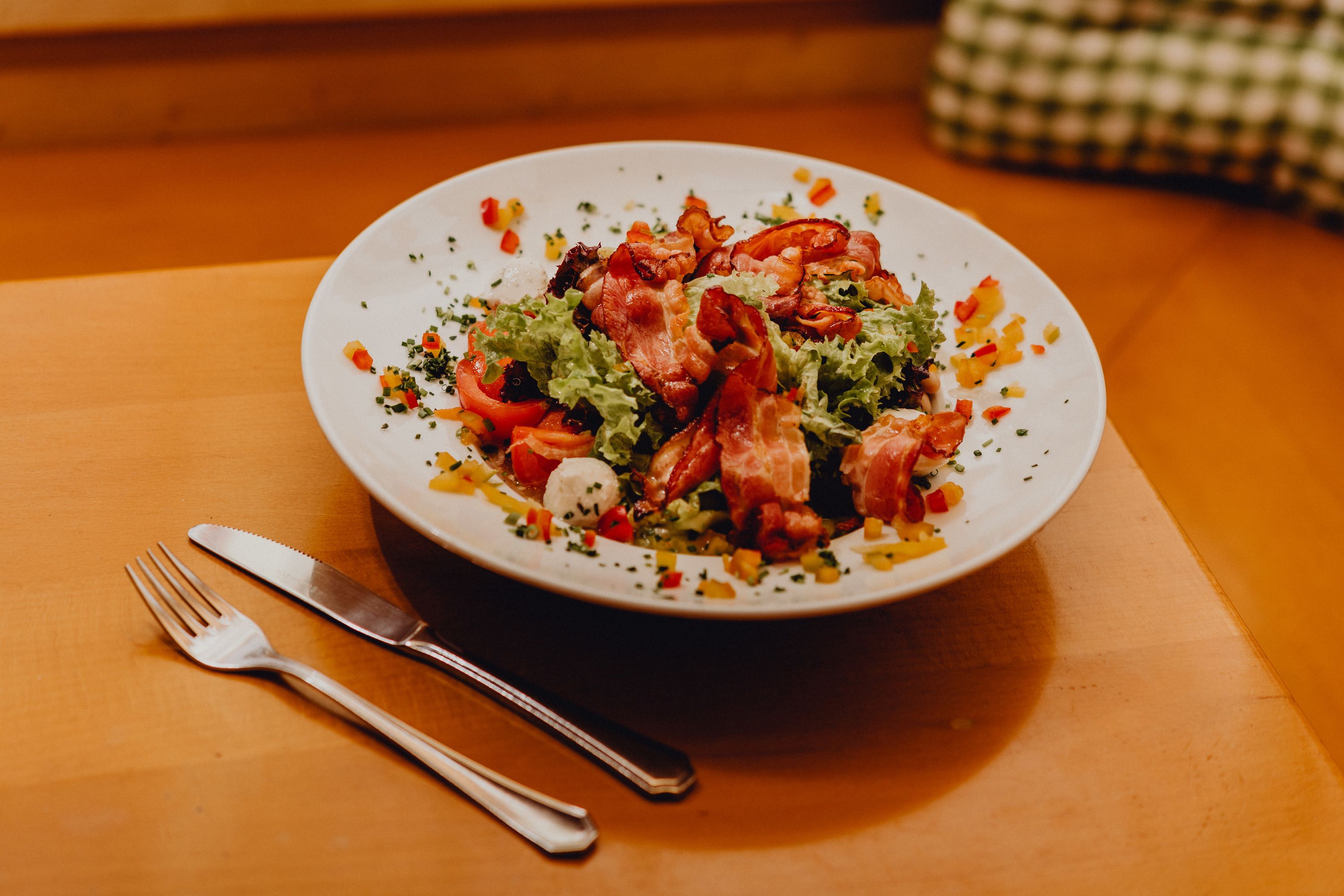 Ein Teller mit gemischtem Salat, Ziegenkäse und Speck auf einem Holztisch.