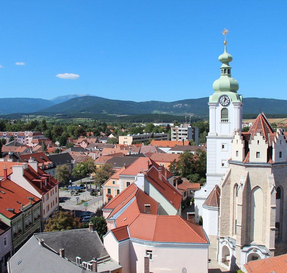 Ausblick auf Neunkirchen mit Häusern, Kirche und Bergen im HIntergrund.