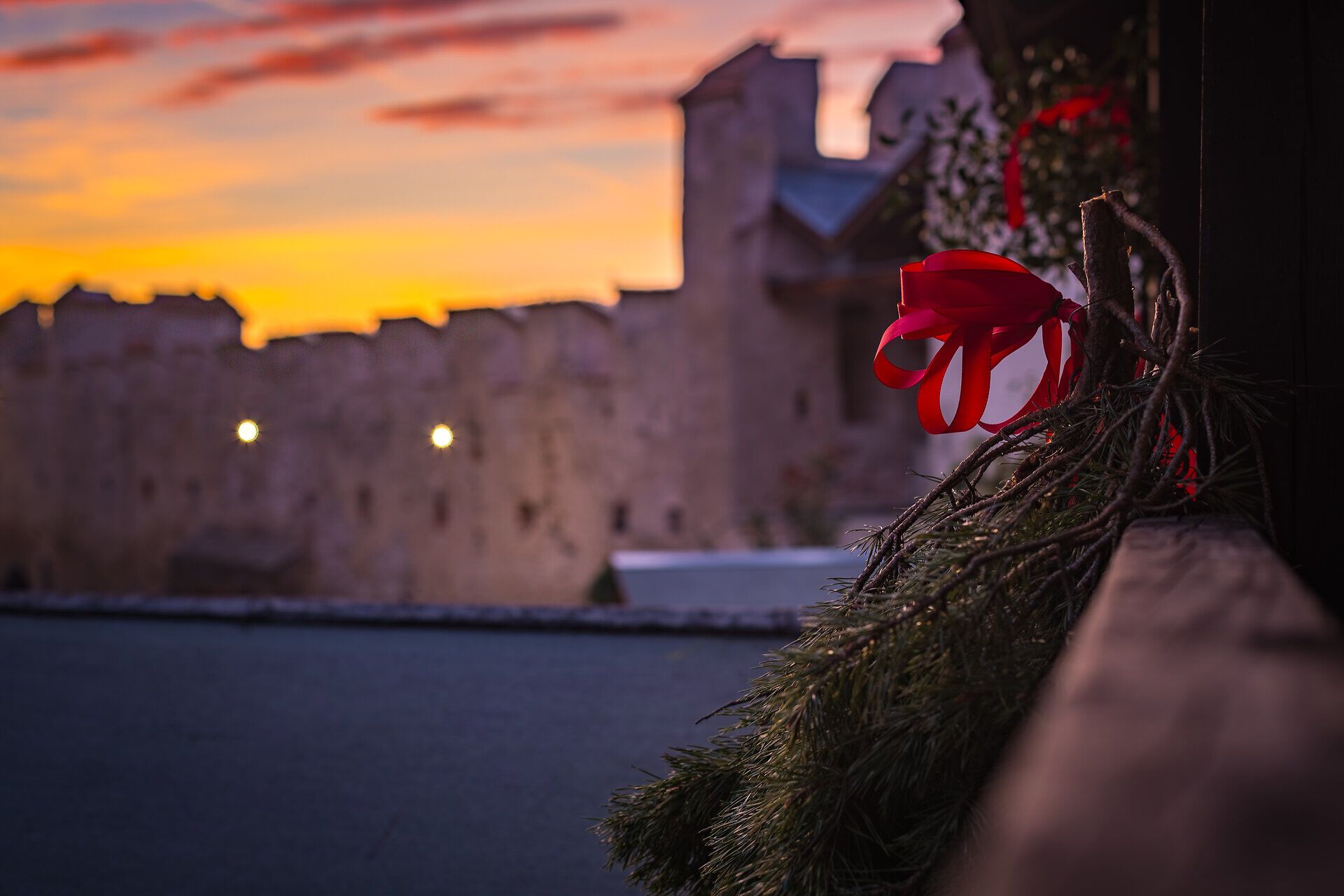 Weihnachtlicher Tannenzweig mit roter Schleife vor einer Burg bei Sonnenuntergang.