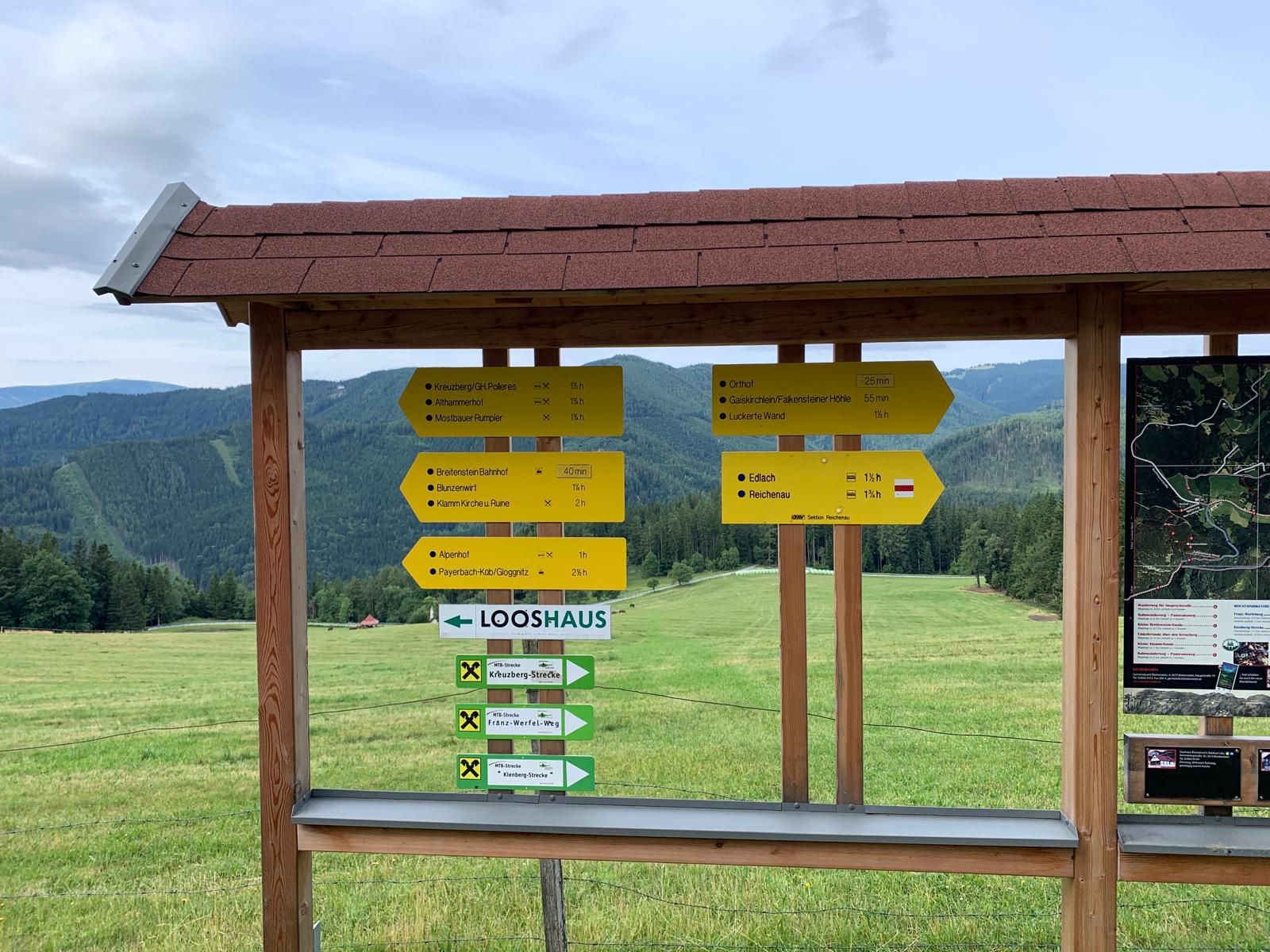 Signpost with yellow signs on a meadow in front of a mountain landscape.