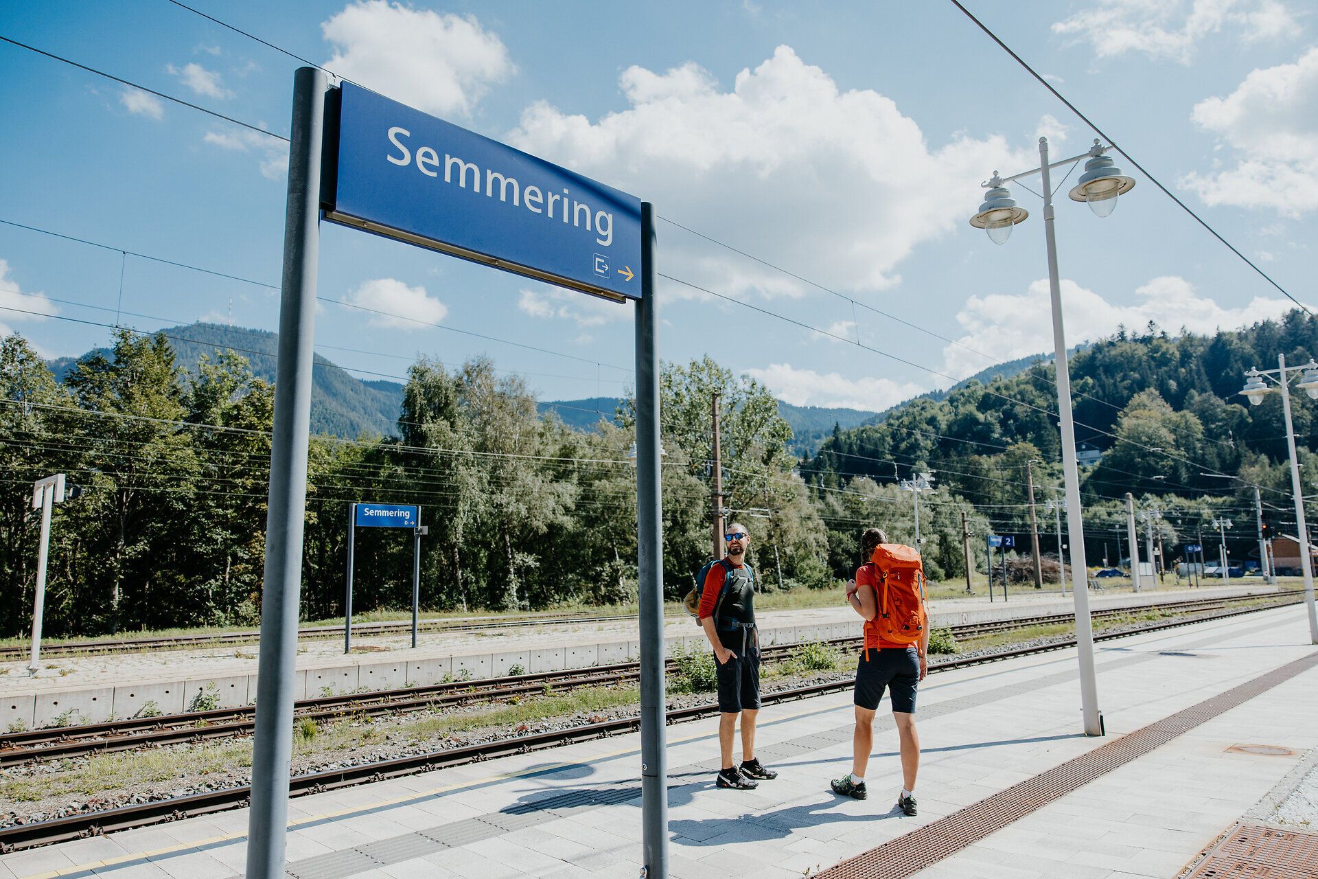 Die Sonne strahlt über die sanften Hügel, während Wanderer mit Rucksäcken die frische Bergluft genießen. Umgeben von üppigem Grün und majestätischen Bergen, lädt die Umgebung zu unvergesslichen Erlebnissen ein. Der Weg verspricht atemberaubende Ausblicke und die Möglichkeit, die Schönheit der Natur hautnah zu erleben.