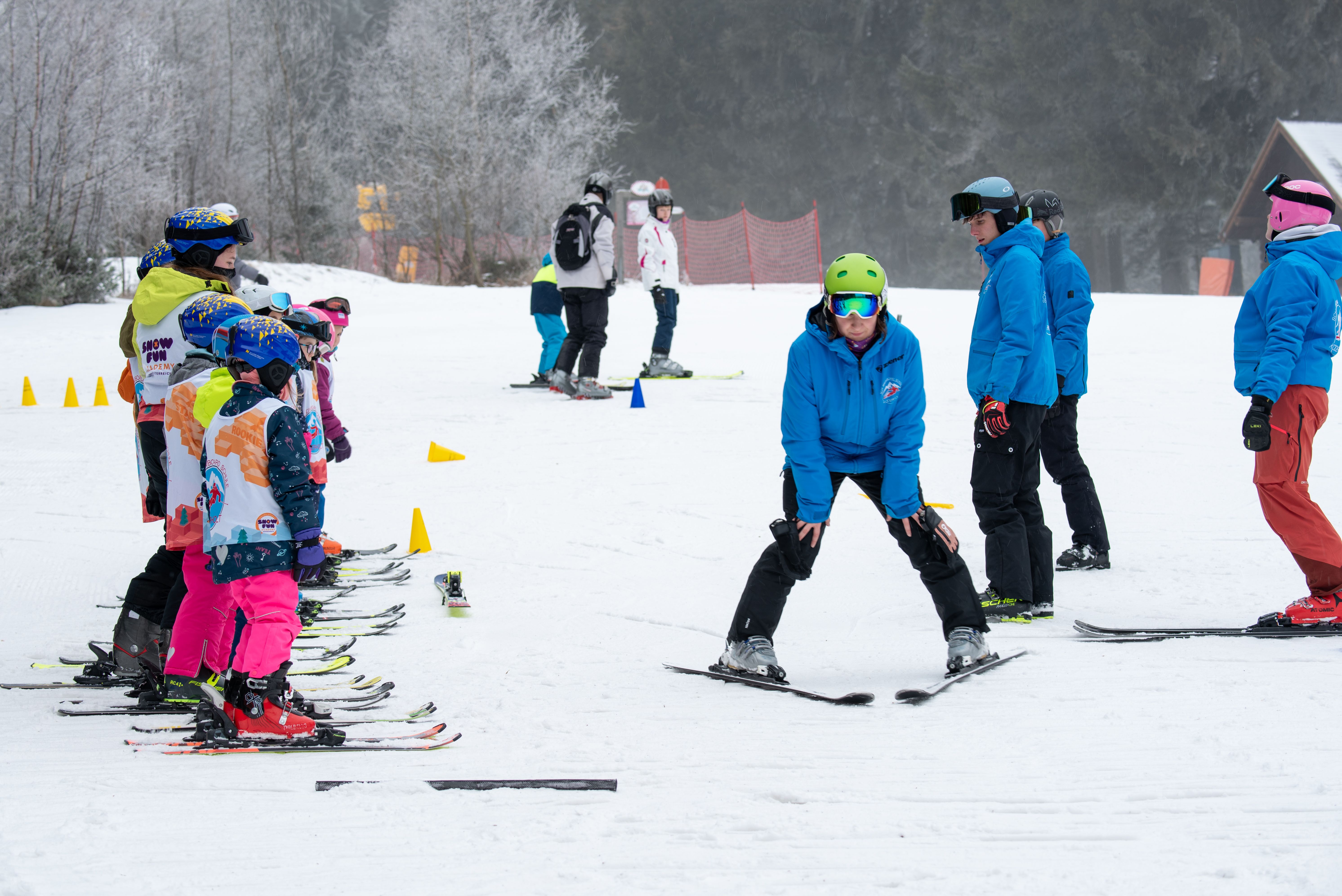 Skilehrer zeigt Kindern auf Skiern eine Übung auf einer Skipiste.