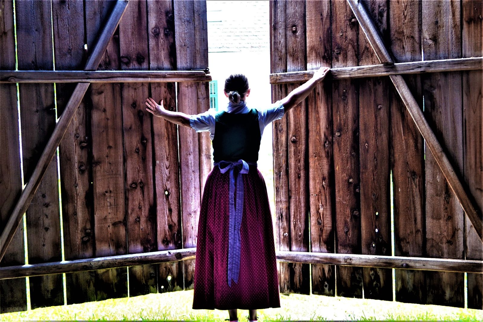 Eine Frau in traditioneller Kleidung öffnet große Holztüren nach außen.