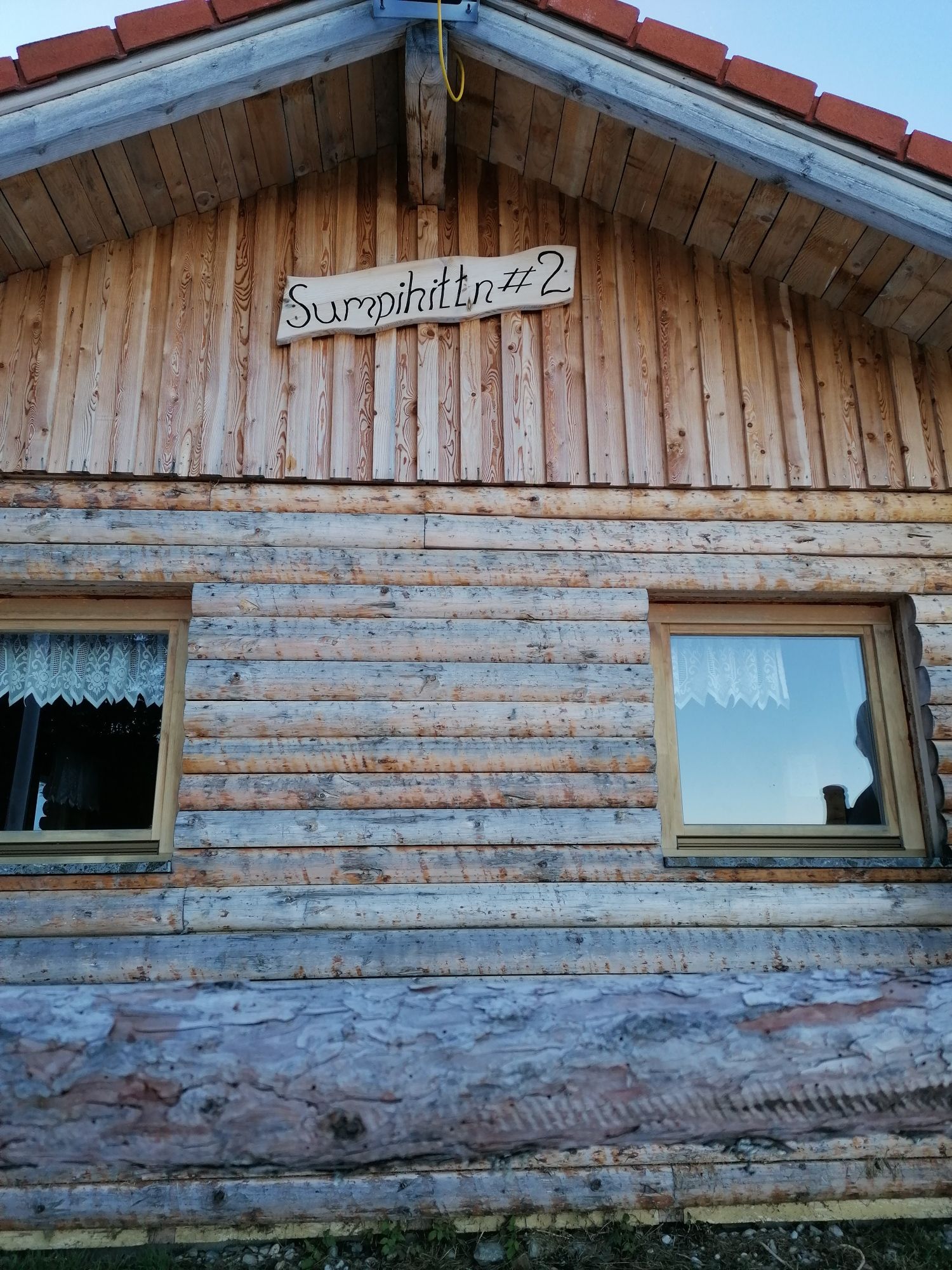 Holzhütte mit der Aufschrift 'Sumpihittn #2' über den Fenstern.