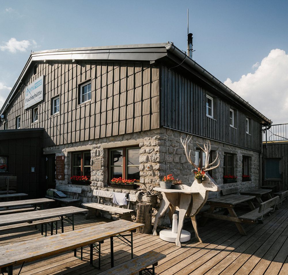 Fischerhütte am Schneeberg mit Terrasse, Sitzbänken und dekorativer Steinbockfigur vor dem Gebäude
