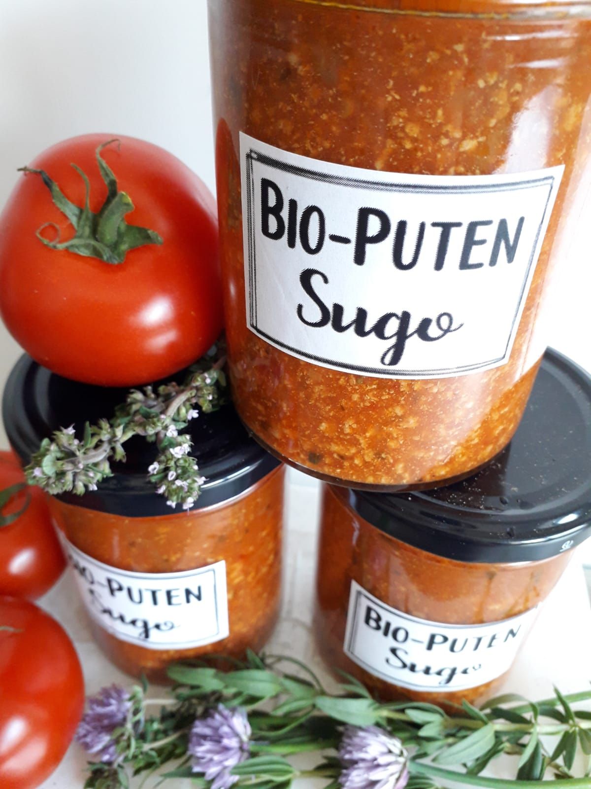 Gläser mit Bio-Puten Sugo, daneben Tomaten und Kräuter.