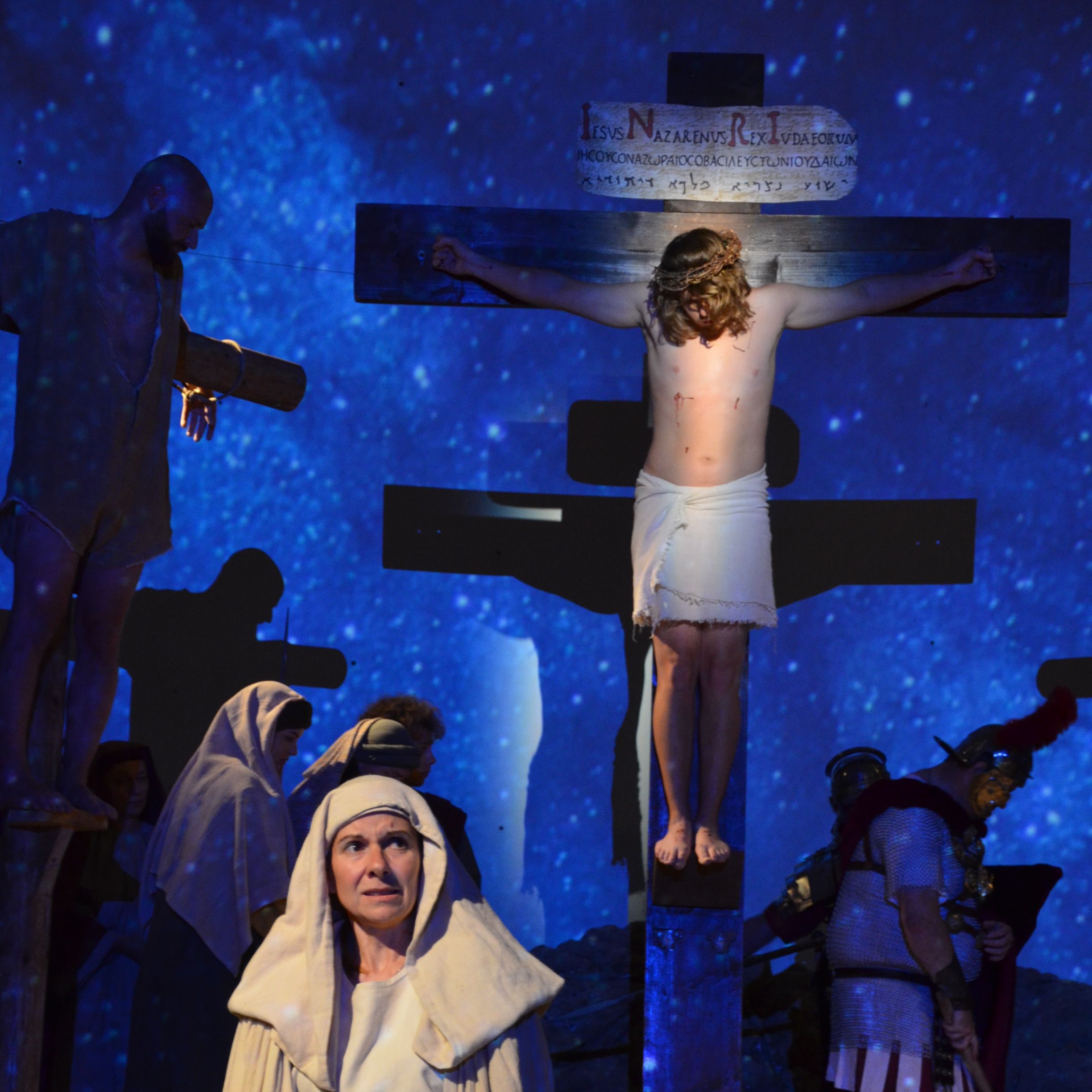 Szene aus den Passionsspielen: Maria steht in Abendlicht vor dem Kreuz, an das Jesus genagelt wurde. Im Hintergrund sind weitere Personen sichtbar.