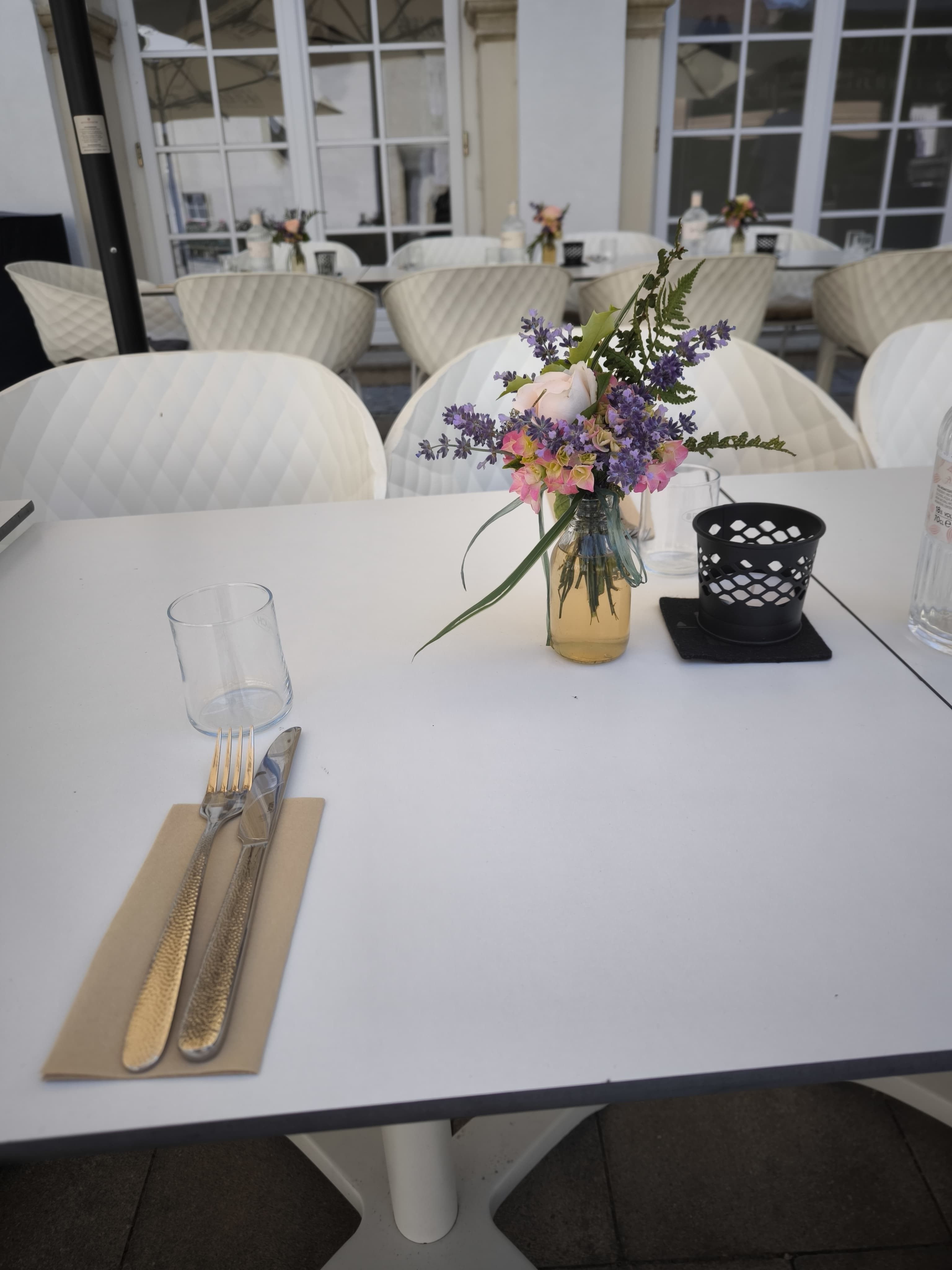 Gedeckter Tisch auf einer Terrasse mit Blumenstrauß und Besteck.