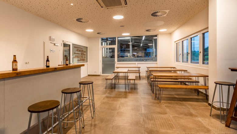 Tasting room of a brewery with wooden tables and benches and a bar with stools.