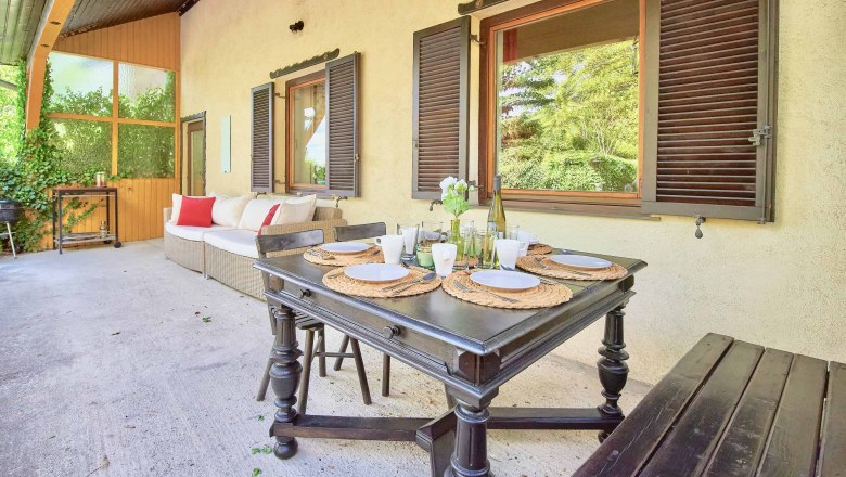 Terrace with dining table, chairs and sofa, surrounded by plants.