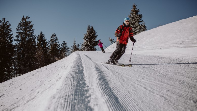 Zwei Skifahrer auf einer präparierten Piste im Schigebiet Unterberg.