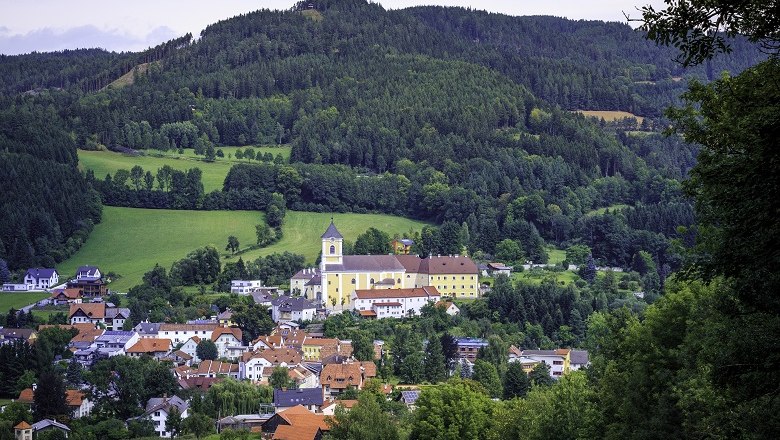 Eine Kirche thront über einem malerischen Dorf, umgeben von grünen Hügeln und Wäldern.